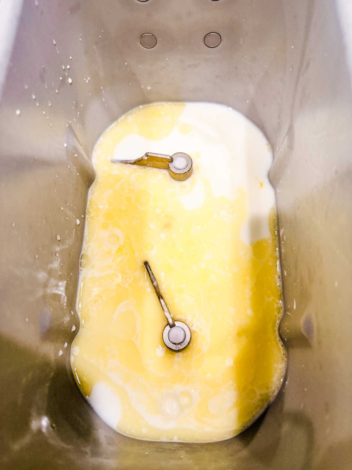 Bread machine pan with two kneading paddles, filled with a mixture of milk and melted butter, ready for baking.