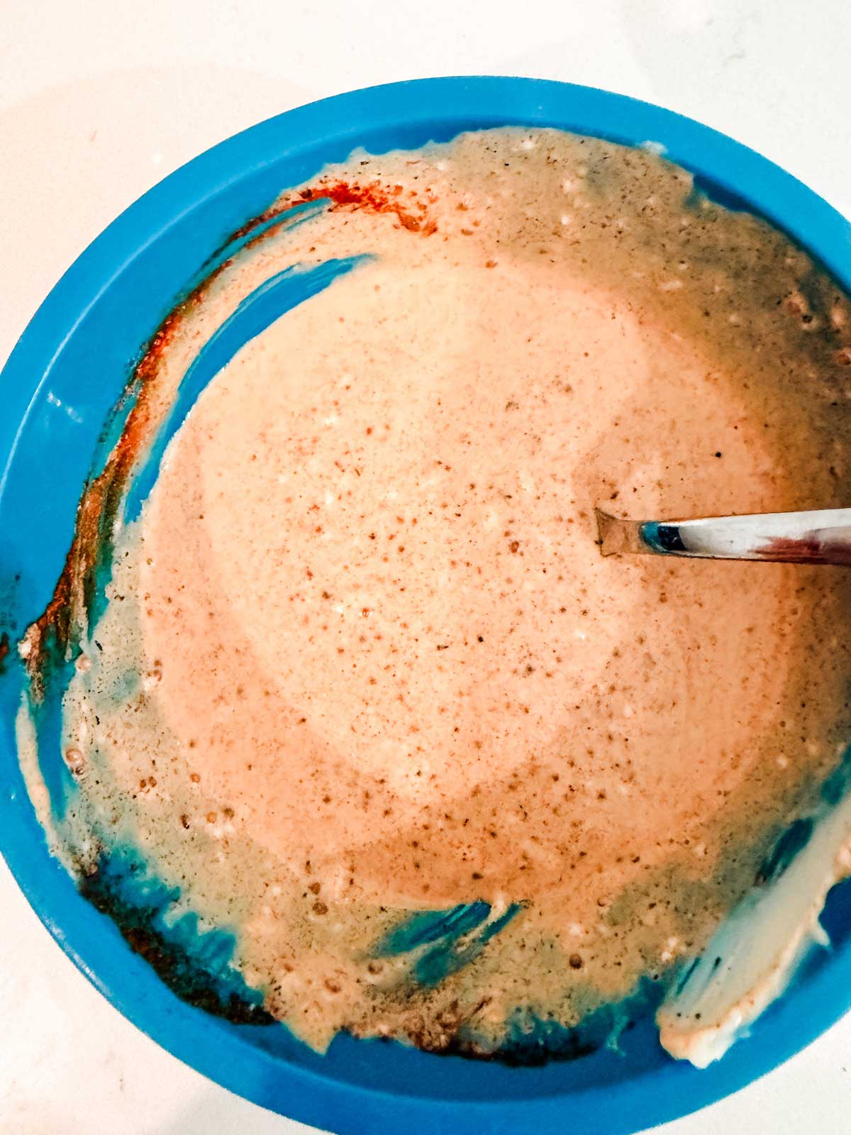 A blue bowl filled with cajun coleslaw dressing. A metal spoon is partially submerged in the mixture.