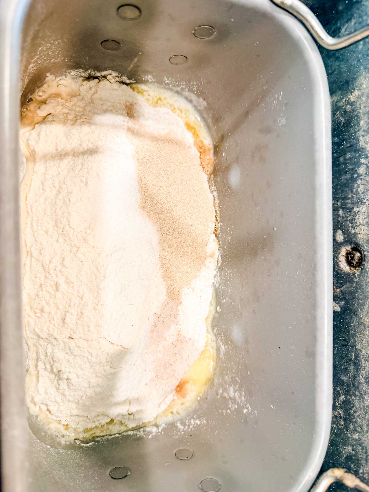 A close-up of a bread machine pan containing layers of flour, yeast, and other ingredients before mixing.