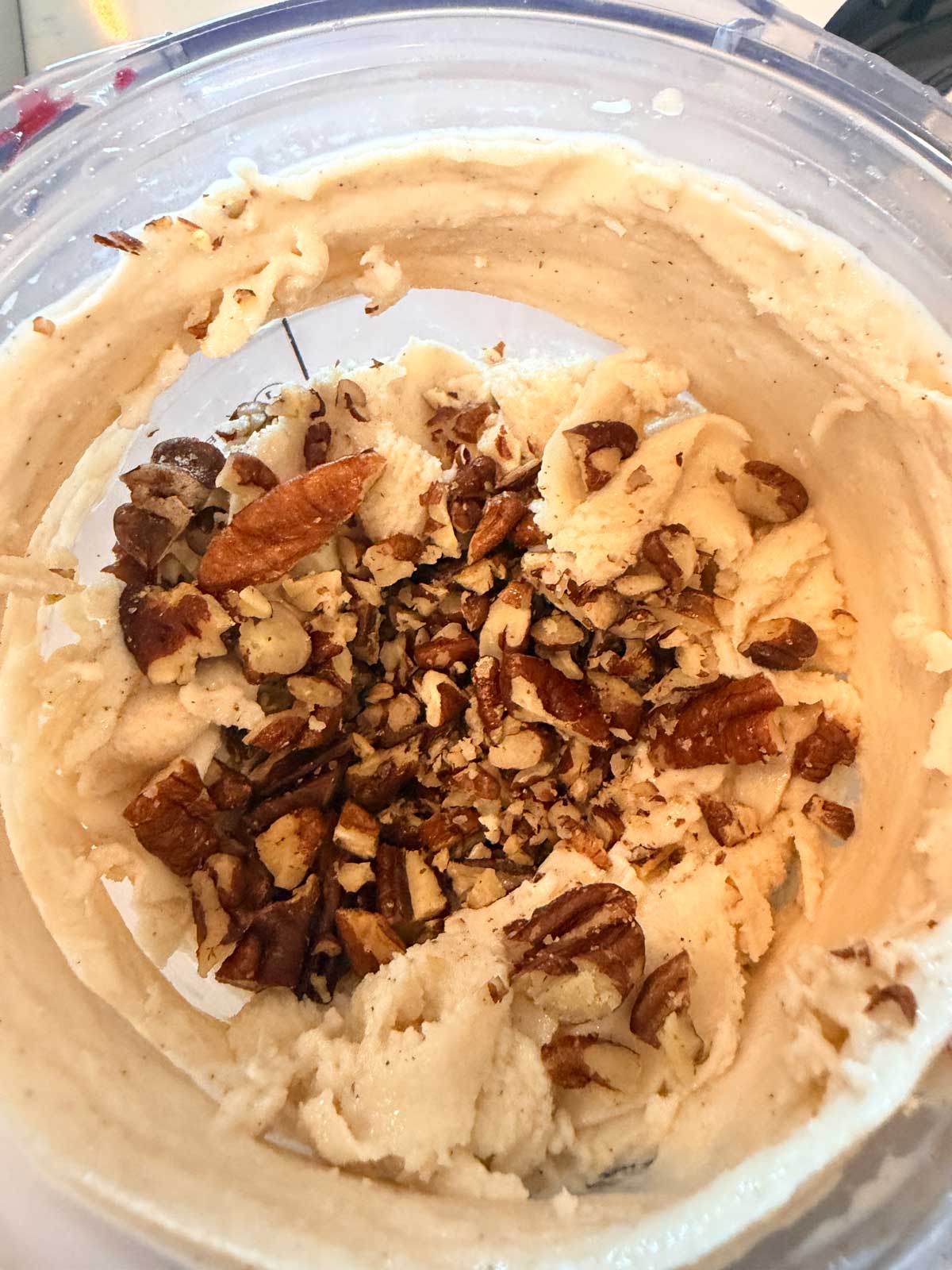 A close-up shot of creamy ice cream in a mixing bowl, topped with a pile of chopped pecans in the center.
