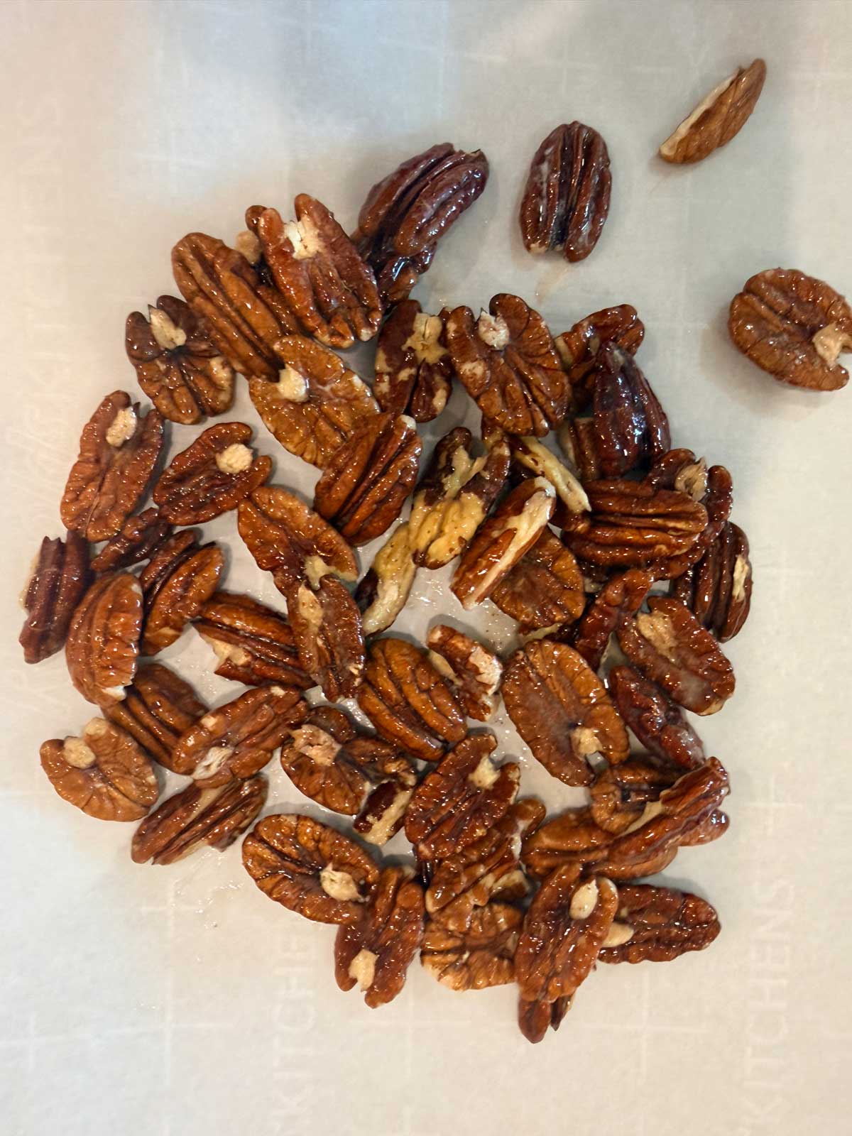 A cluster of glazed pecan halves spread out on a sheet of parchment paper.