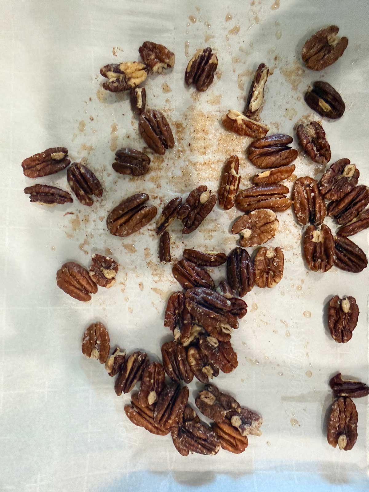 Pecan halves scattered on a sheet of parchment paper, sprinkled with brown sugar and a light glaze.