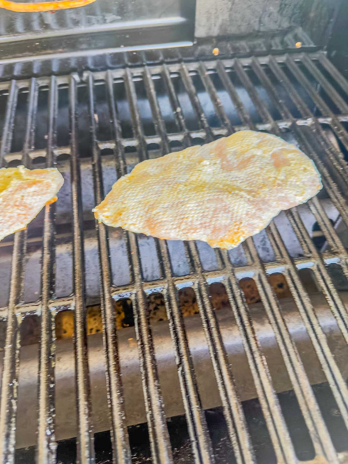 A piece of seasoned fish fillet is being grilled on an outdoor barbecue grill with visible grill marks forming on the fish.