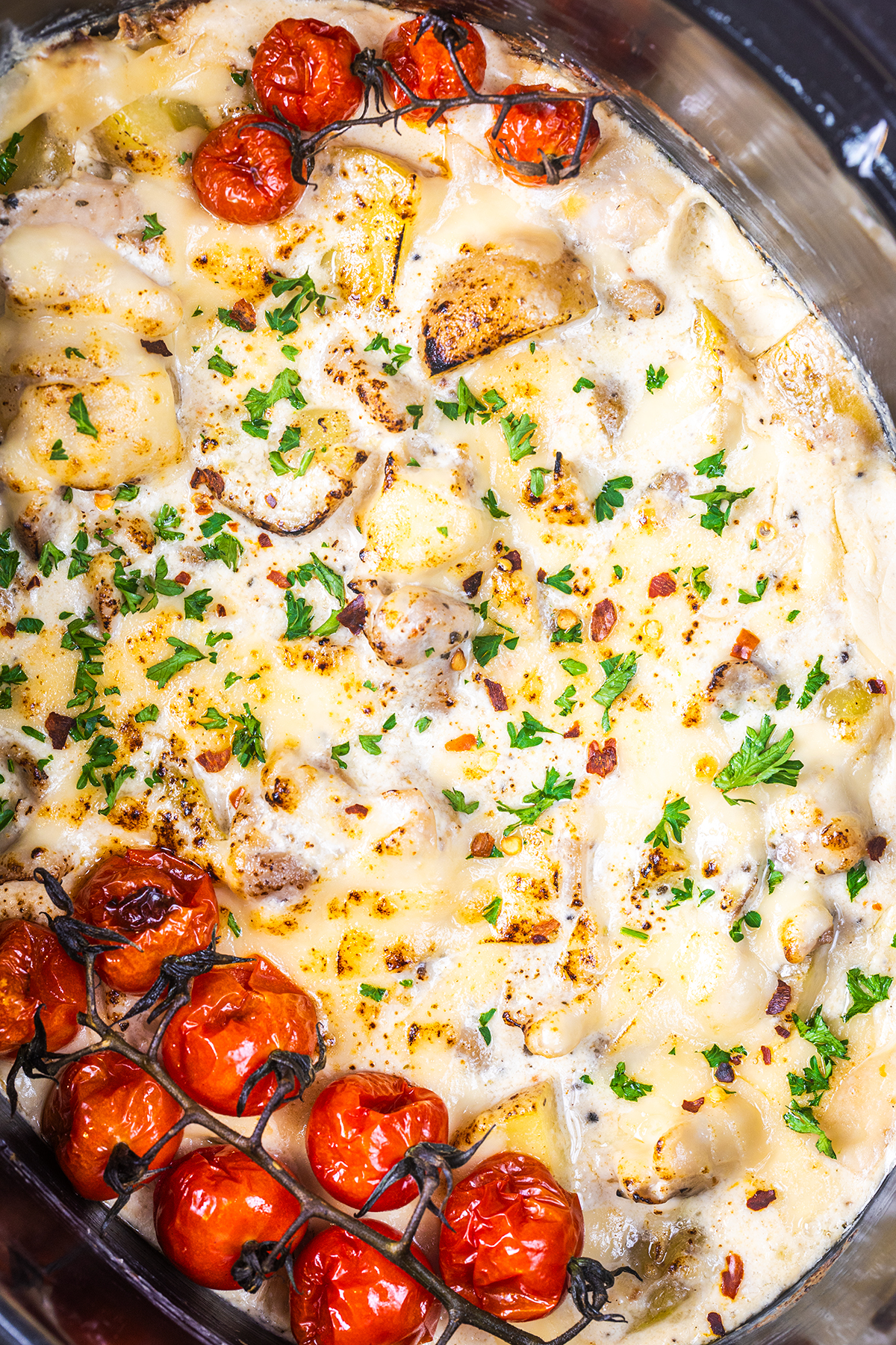 Creamy crockpot Italian chicken topped with melted cheese, fresh parsley, and roasted cherry tomatoes on the vine, all in a slow cooker.