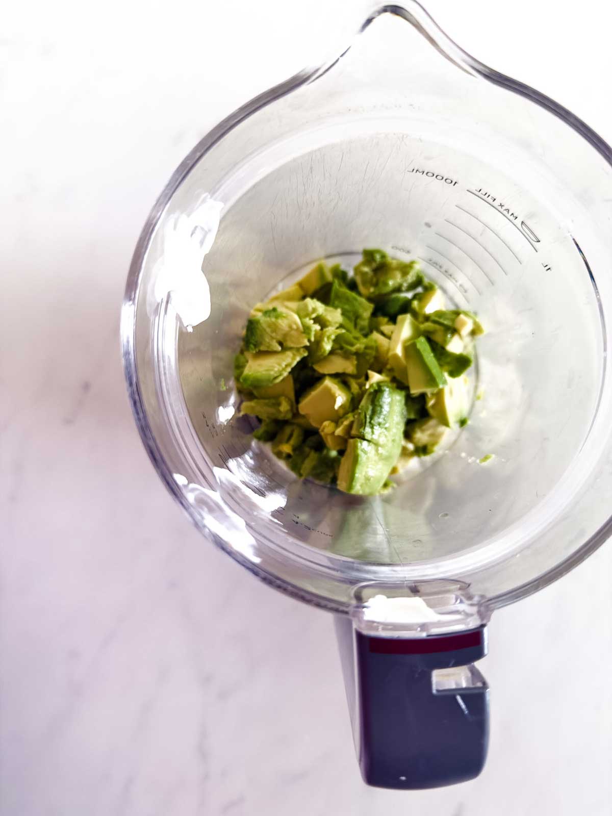 A top-down view of a blender pitcher containing chunks of avocado on a white surface.