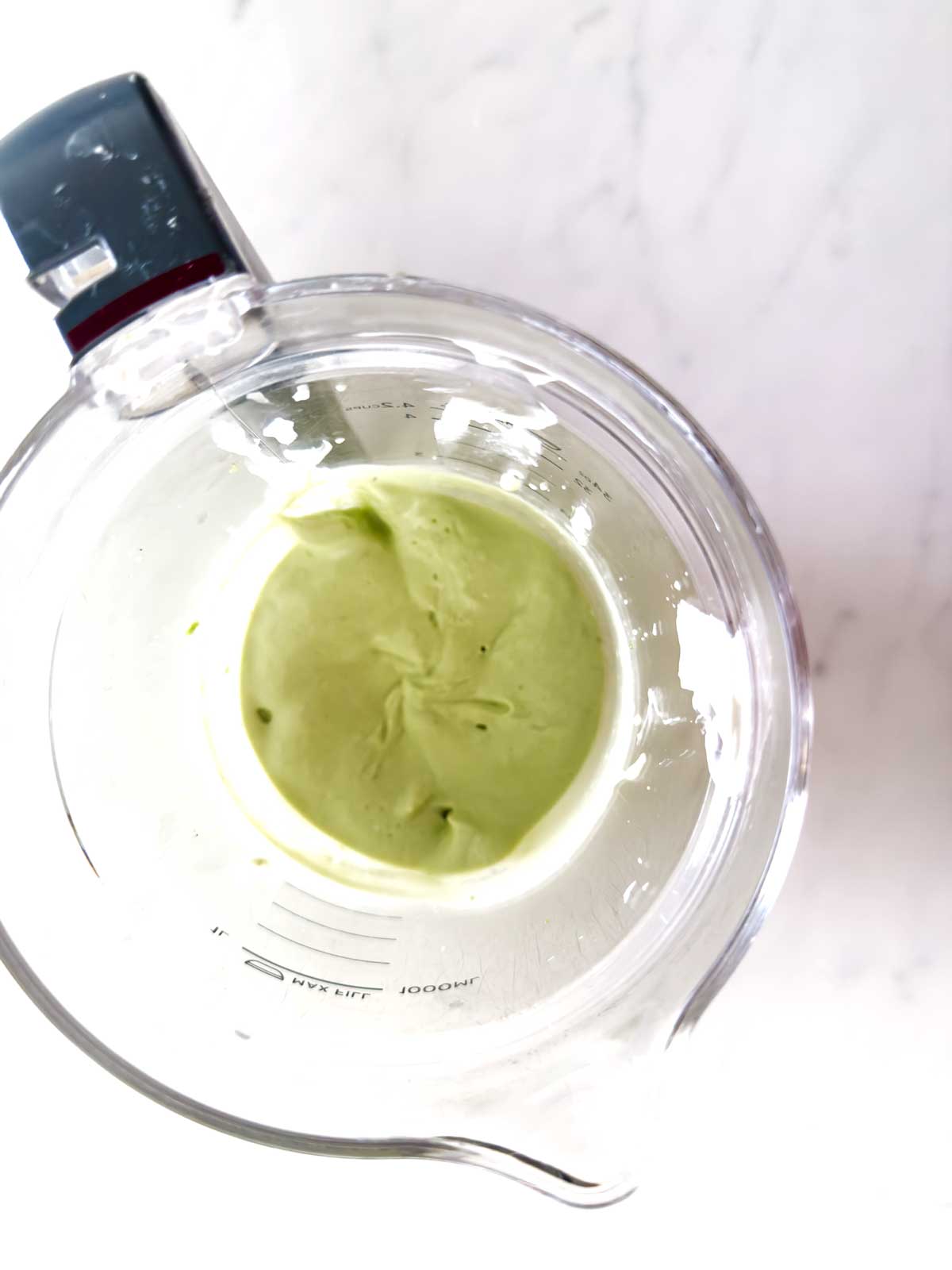 A blender with a pale green creamy mixture inside, viewed from above on a white marble surface.