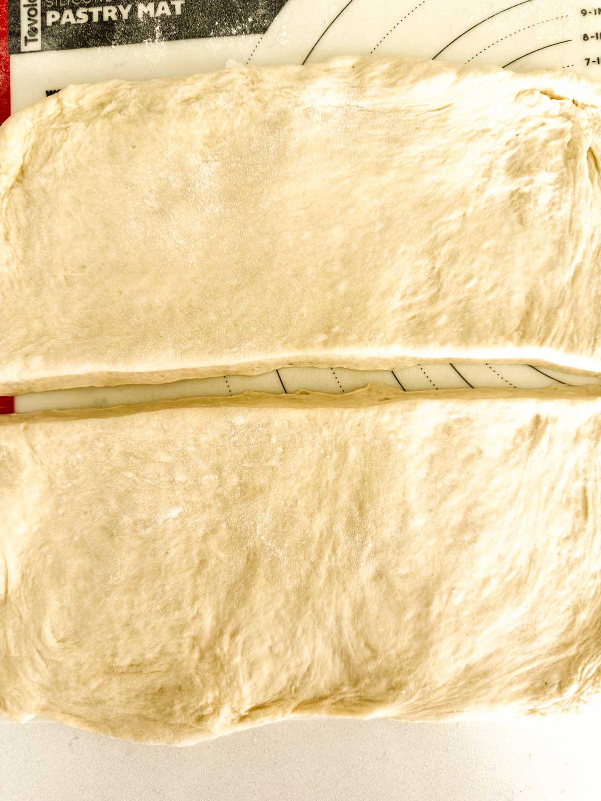 Two rectangular pieces of rolled-out dough sit side by side on a lightly floured surface, ready for baking or further preparation. A pastry mat with measurement marks is partially visible underneath.