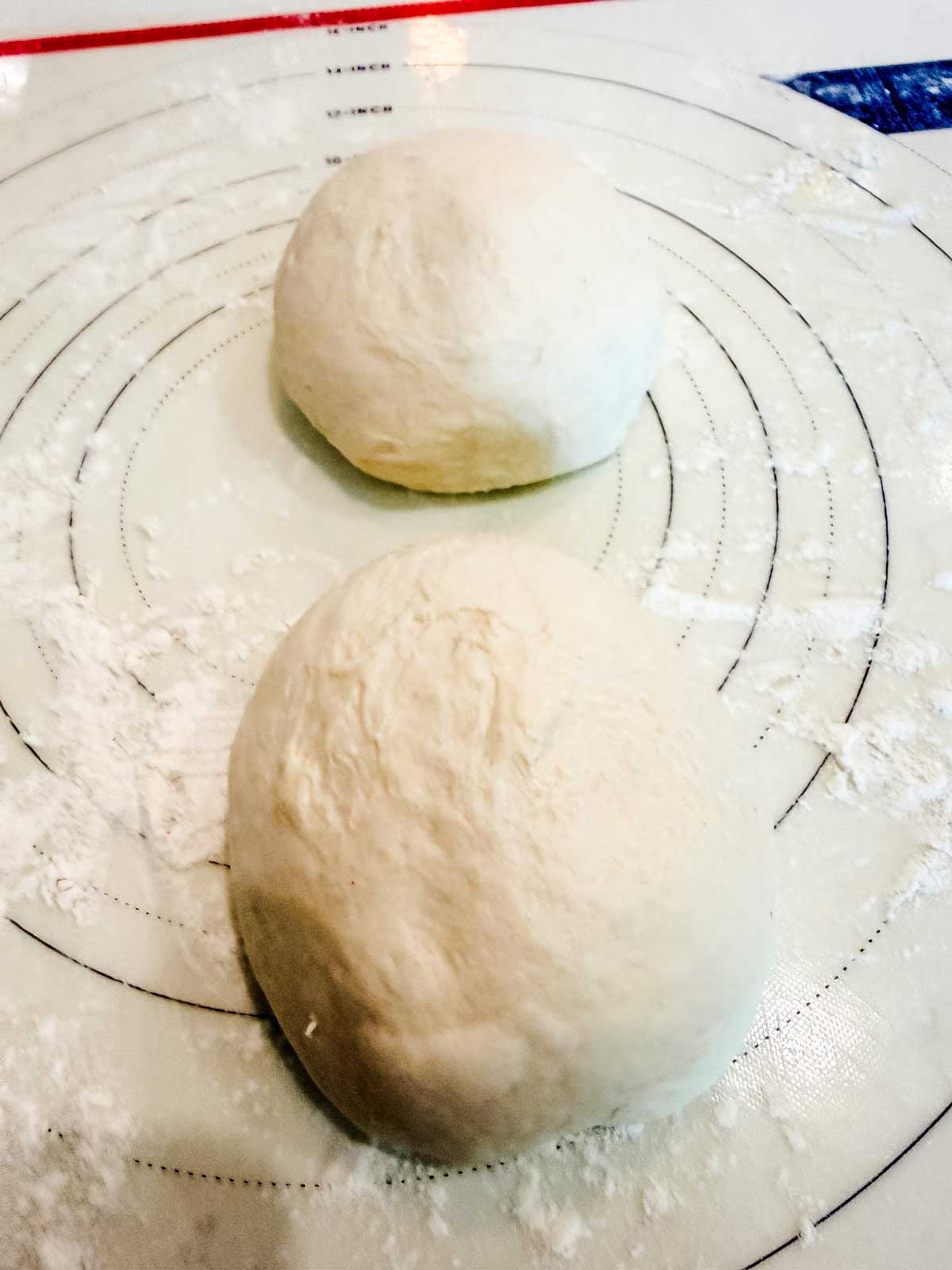 Two balls of dough rest on a floured pastry mat with concentric circles, ready for baking or shaping.