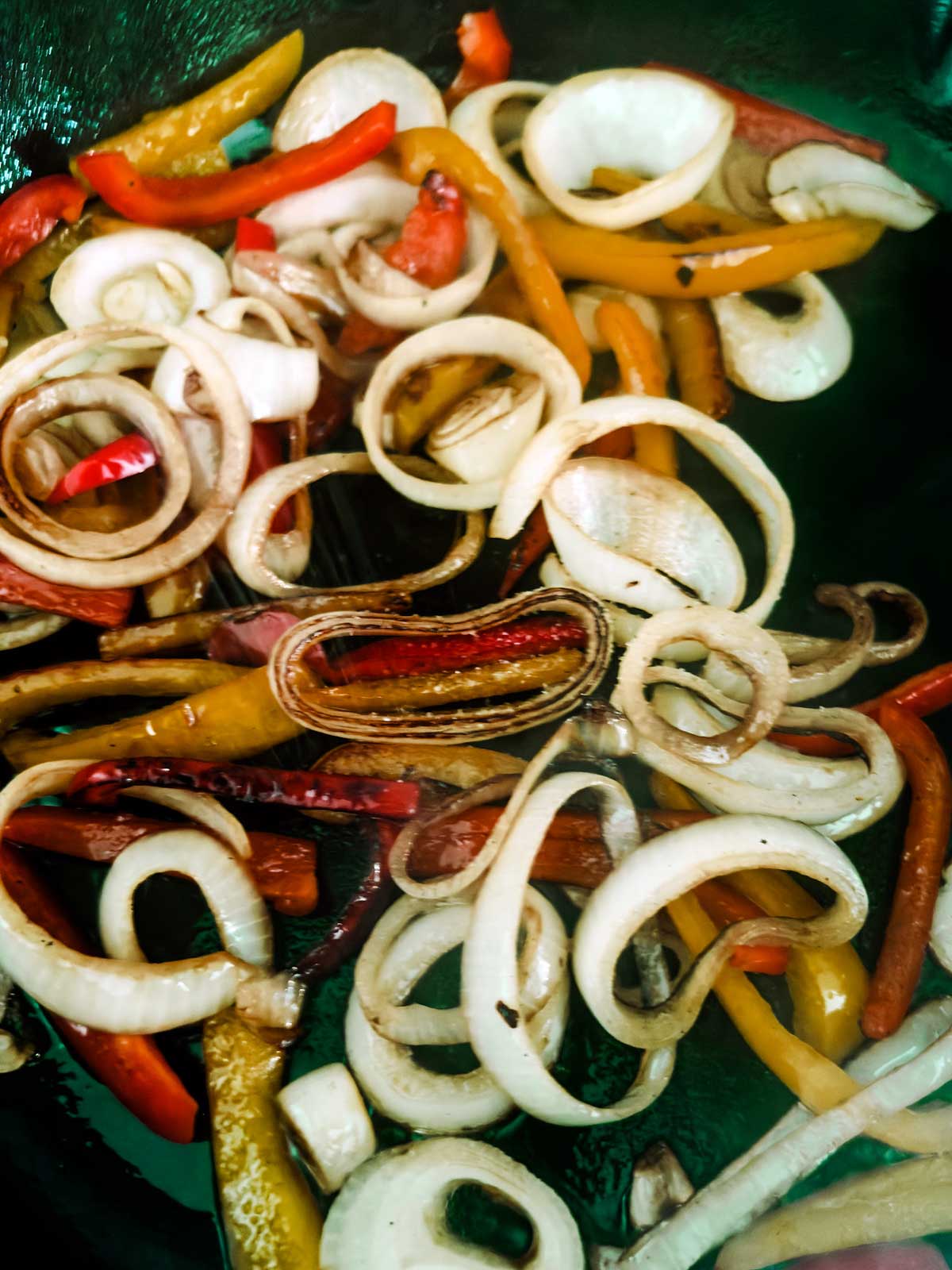 Sliced onions and colorful bell peppers are being sautéed in a pan, with the vegetables visibly starting to soften and caramelize.