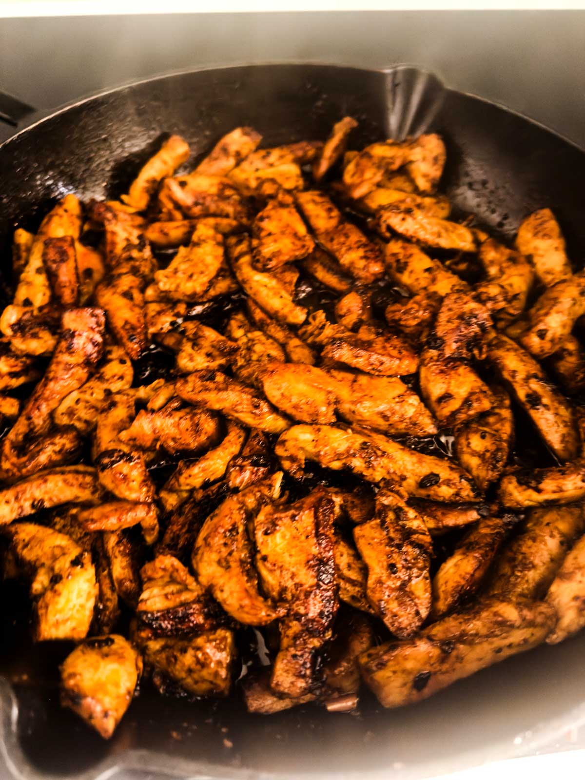 Sliced, seasoned chicken breast pieces cooking in a cast iron skillet, with a dark, flavorful sear on the surface.