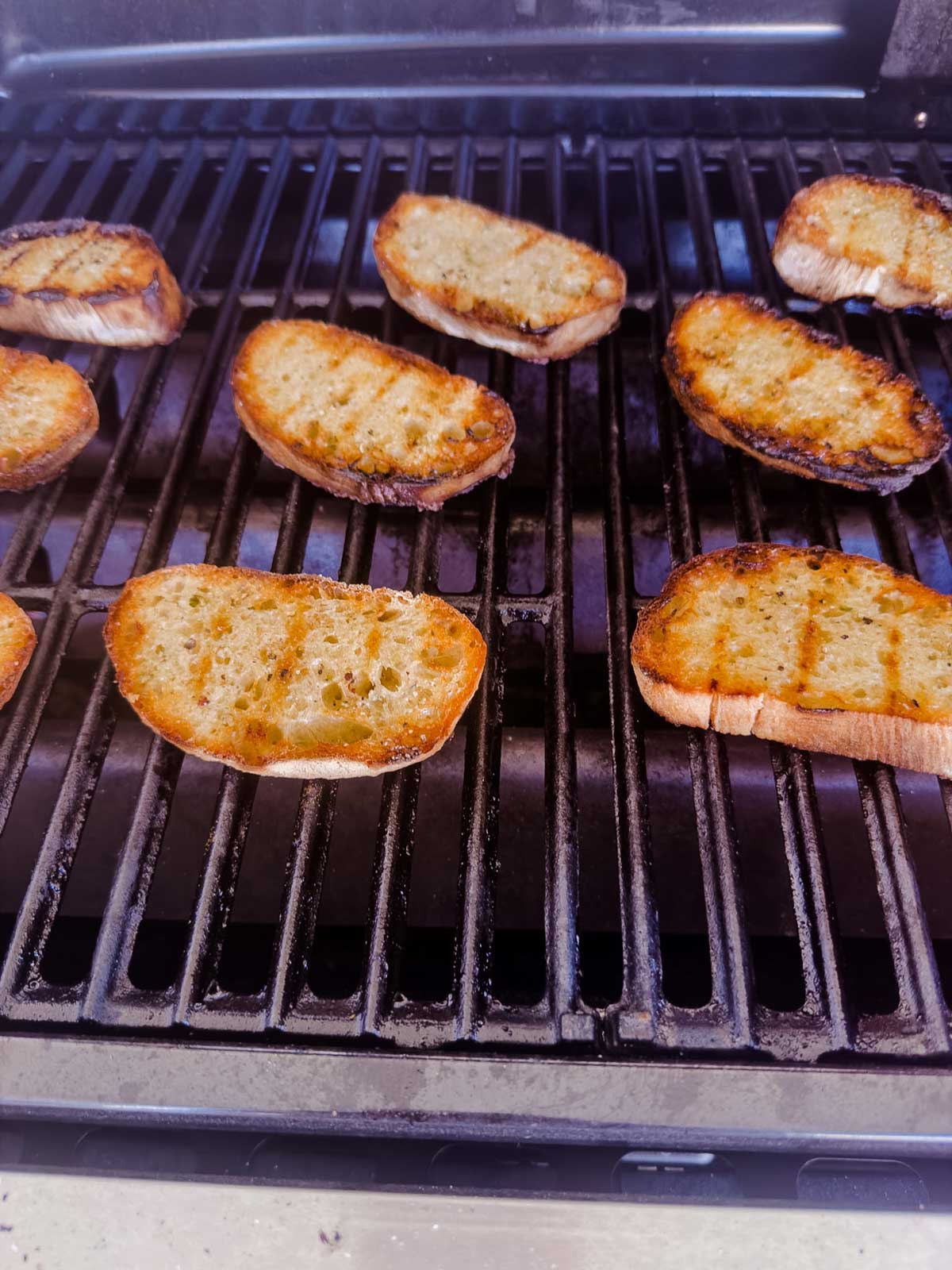 Slices of bread being toasted on a grill, with some pieces showing grill marks and others with slightly charred edges.