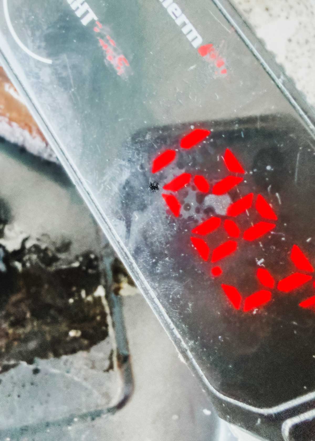 A close-up of a digital kitchen scale displays the red number “222.8” on its screen, with part of a countertop and a stovetop visible in the background.