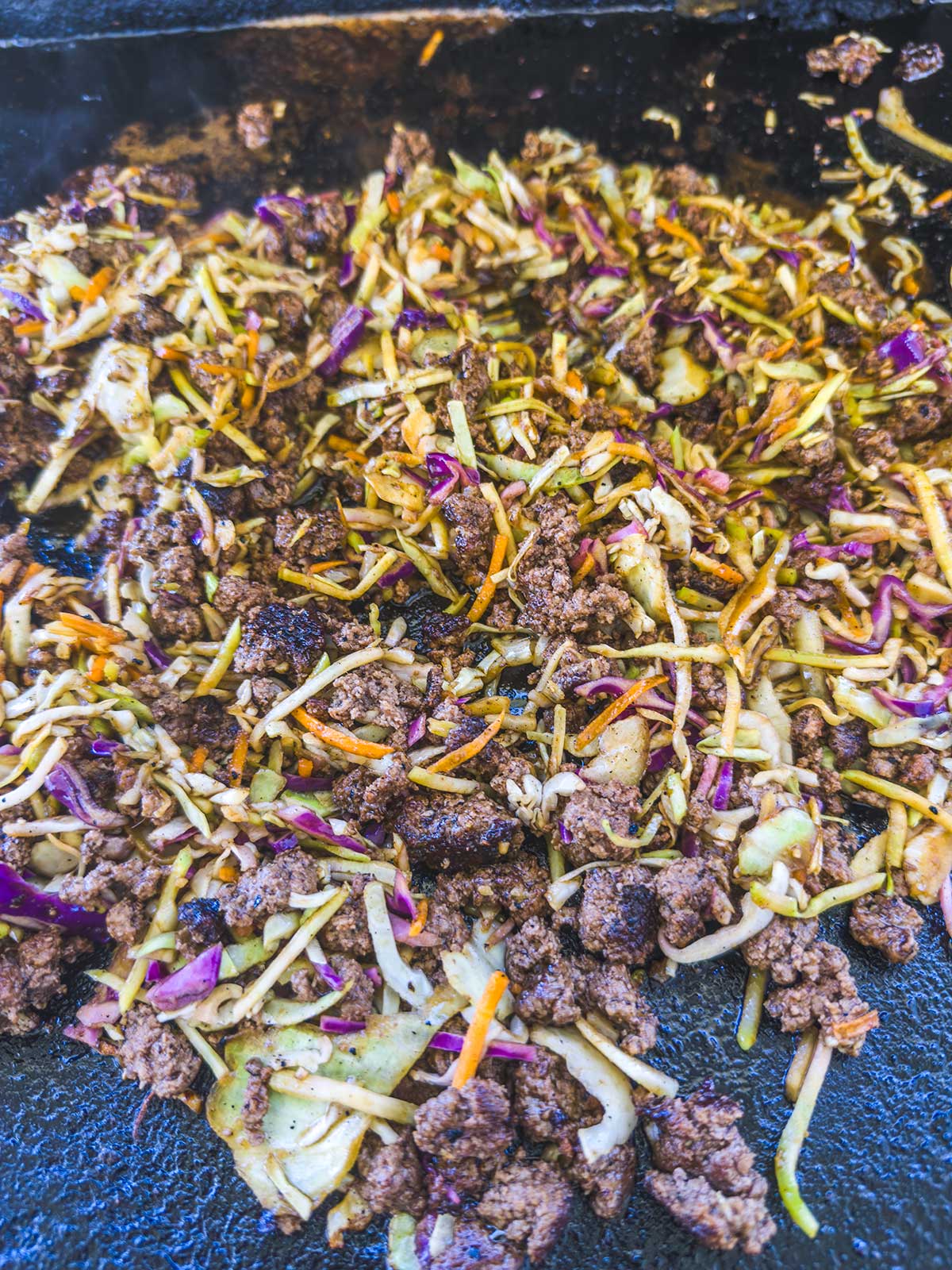 Ground beef mixed with shredded vegetables, including cabbage and carrots, sizzling on the grill—perfect for making a Blackstone egg roll in a bowl.