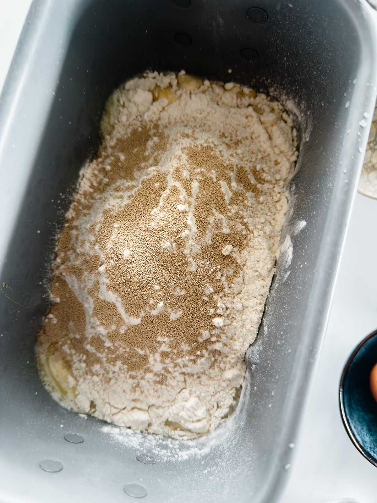 A bread machine pan filled with flour, yeast, and other baking ingredients, ready for mixing.