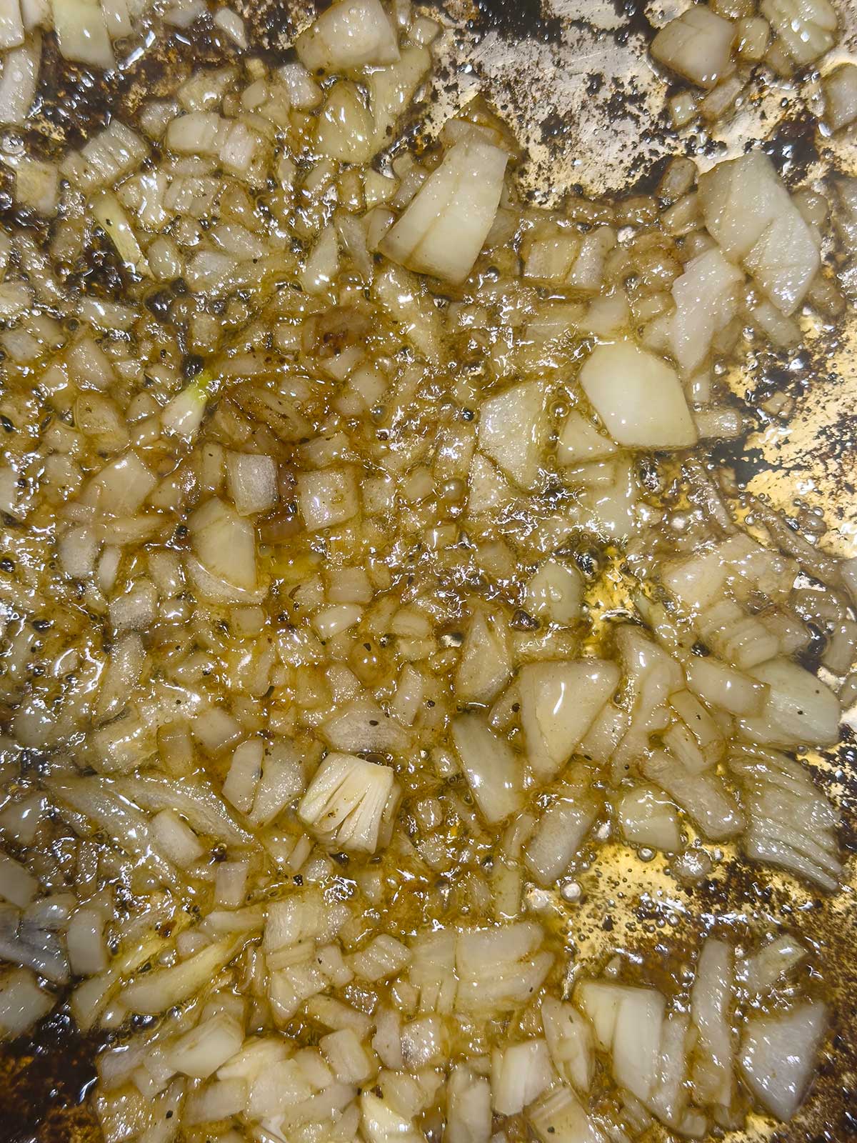 Chopped onions cooking and browning in oil on a stovetop pan, with visible caramelization and golden-brown edges.
