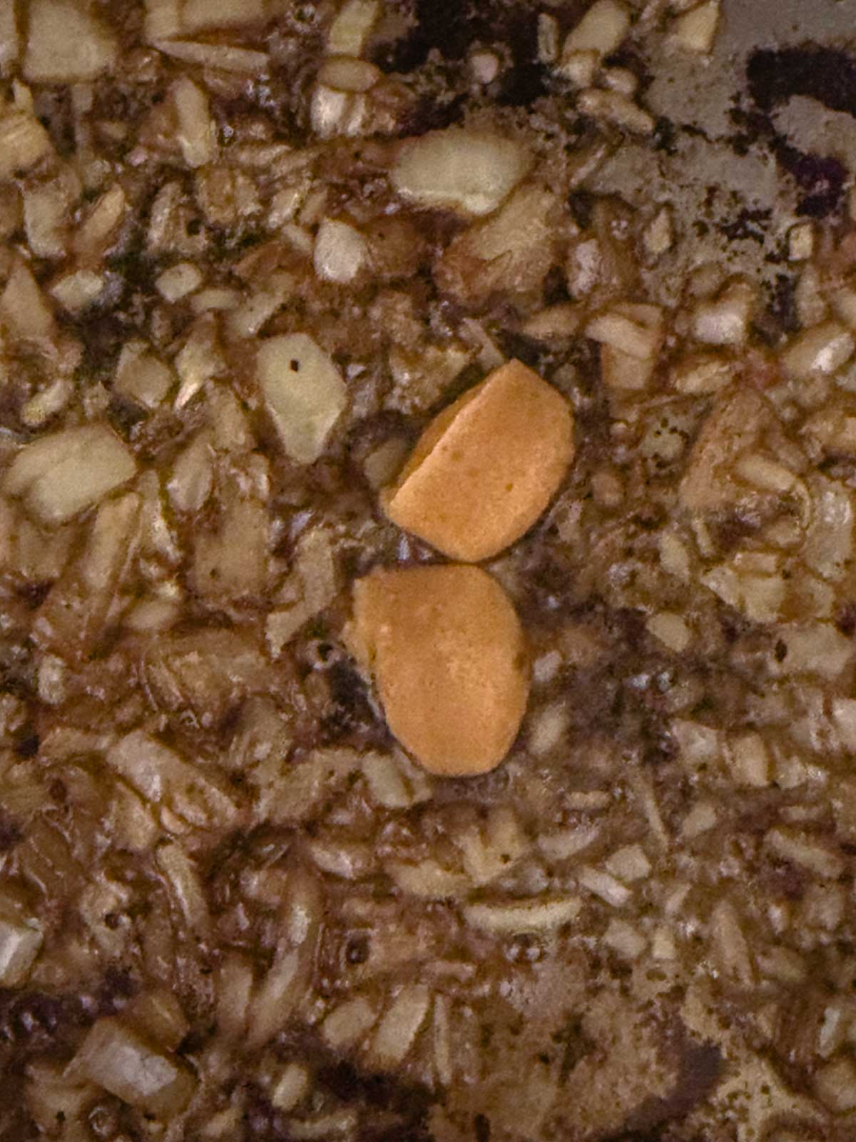 Chopped onions and two pieces of sliced garlic cooking in oil in a pan, starting to brown.