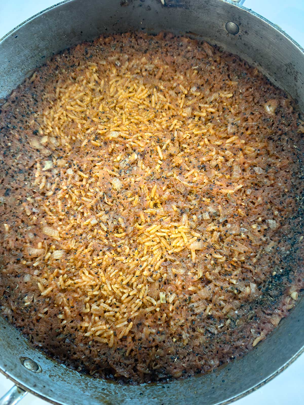 A close-up of a pot filled with burnt rice, showing a layer of dried and scorched rice grains with blackened and brown patches.