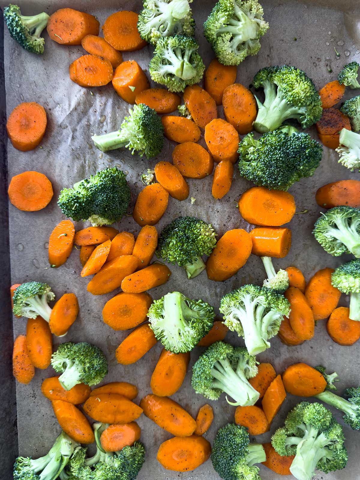 Sliced carrots and broccoli florets spread out on a parchment-lined baking tray, perfect as a base or topping for a flavorful teriyaki chicken bowl.