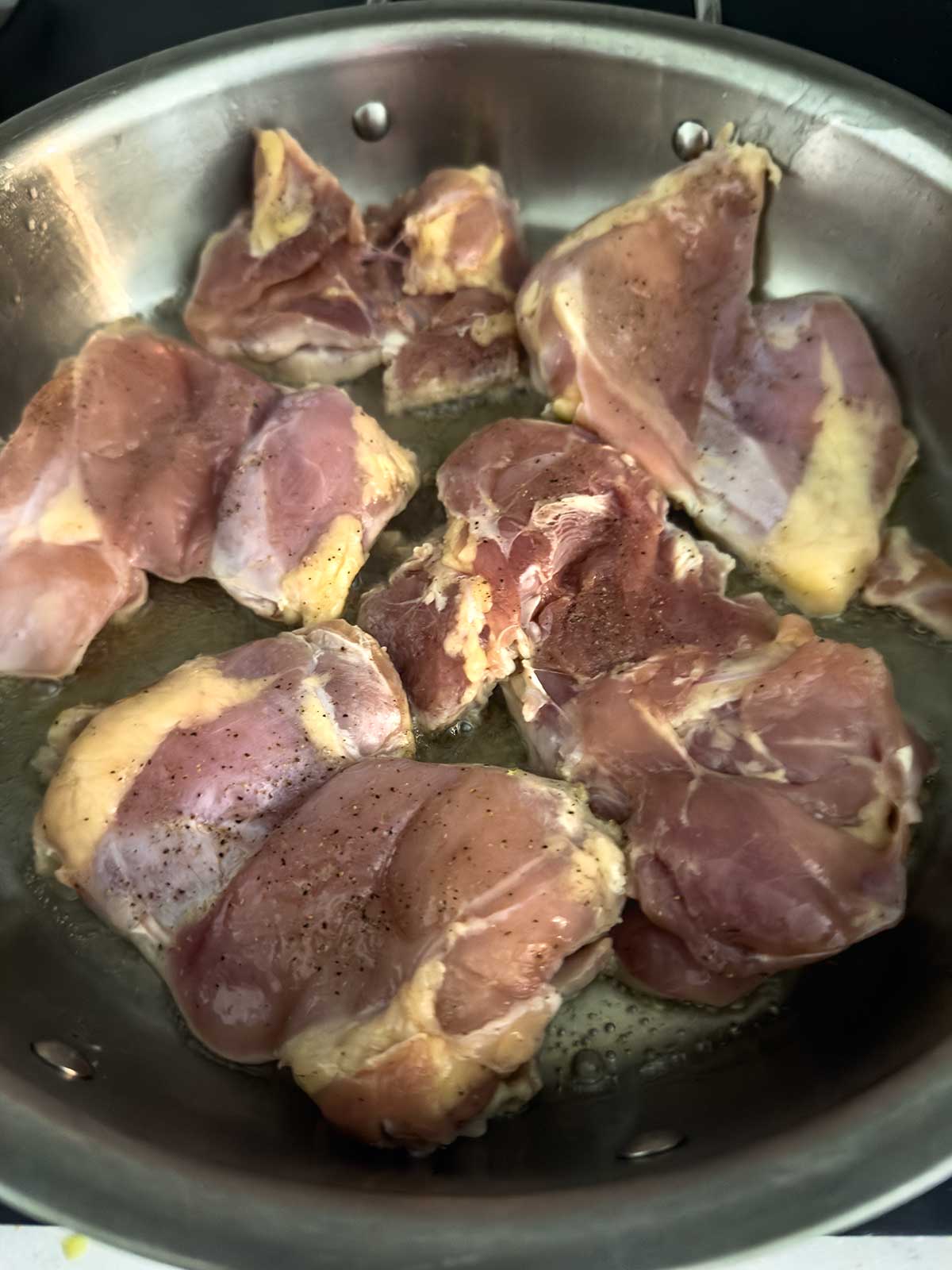 Raw, seasoned chicken pieces cooking in a stainless steel pan over heat, with some oil visible at the bottom—perfectly prepped for a delicious teriyaki chicken bowl.