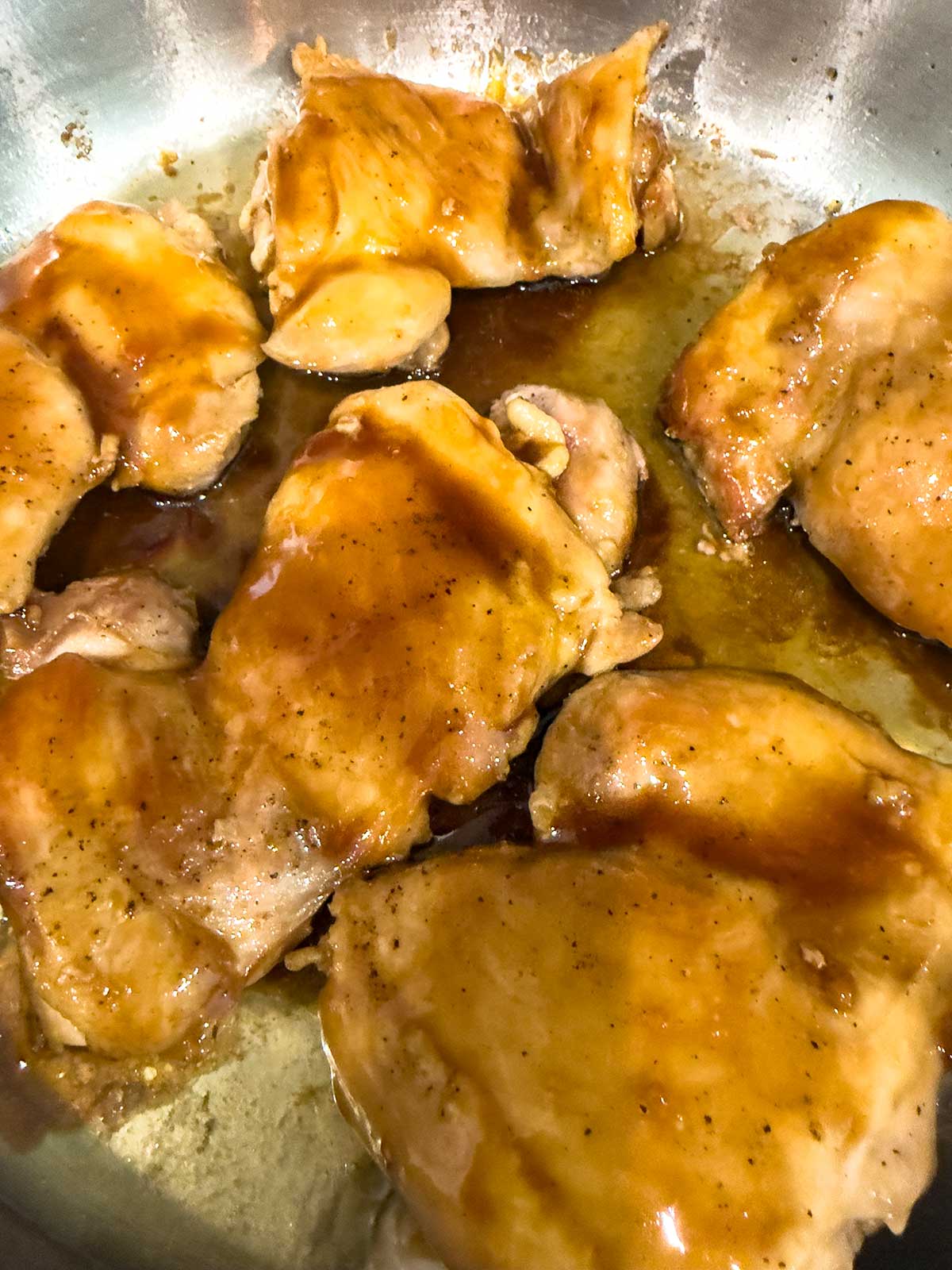Chicken pieces simmering in a pan, coated with a glossy brown sauce, with visible seasoning and caramelization—just like a classic teriyaki chicken bowl. The sauce pools around the chicken, giving it a rich, flavorful appearance.