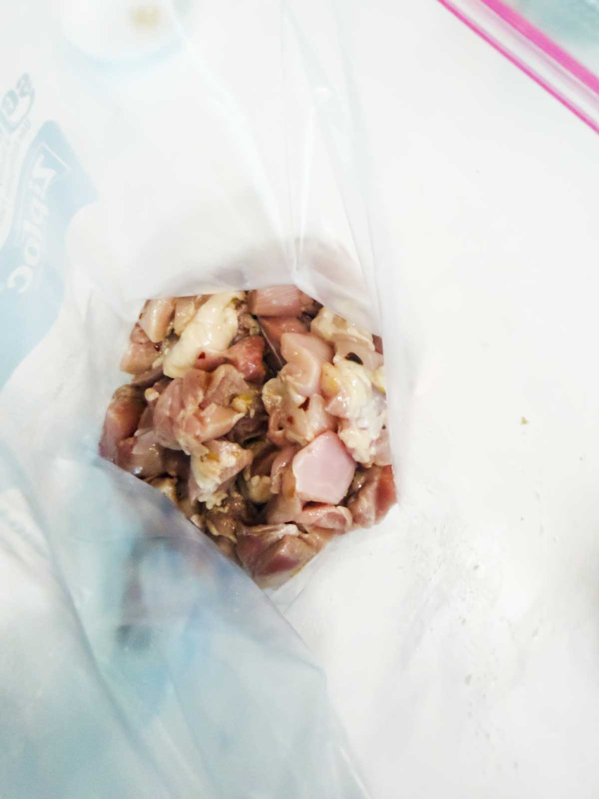 Diced raw chicken pieces inside a partially opened clear plastic zipper bag, set on a white surface.