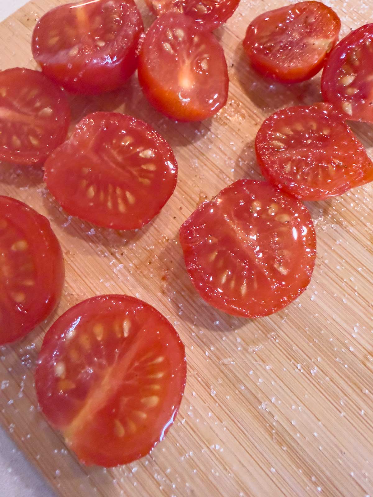Sliced cherry tomatoes, perfect for topping tomato focaccia bread, sprinkled with coarse salt on a light wooden cutting board.