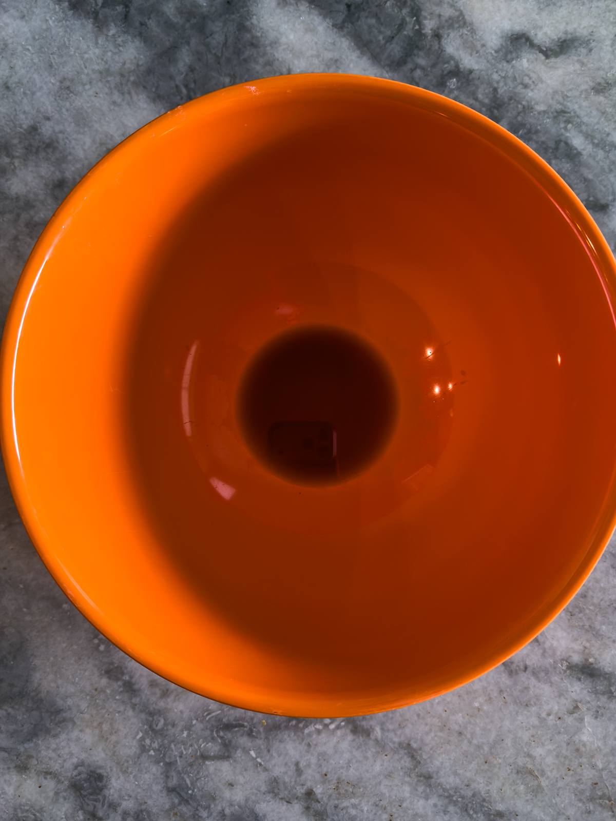 An empty bright orange bowl is placed on a gray marble surface, viewed from above.