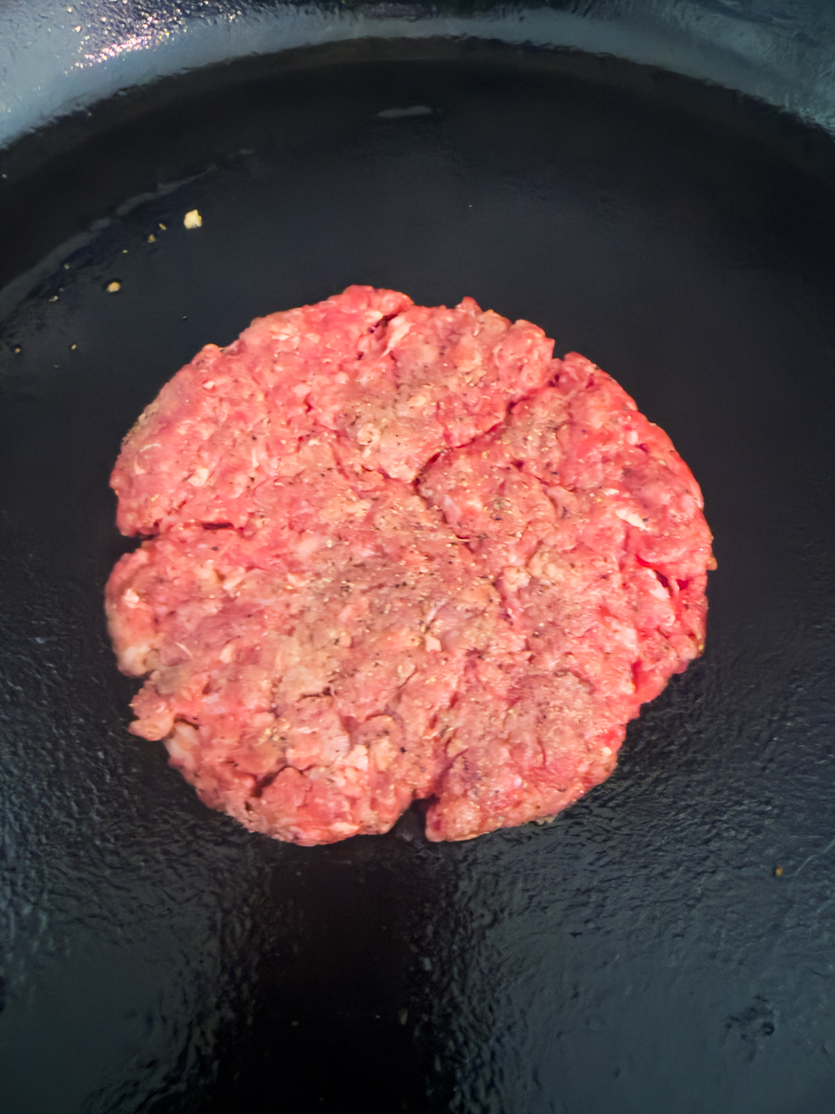 A burger patty in a cast iron skillet.