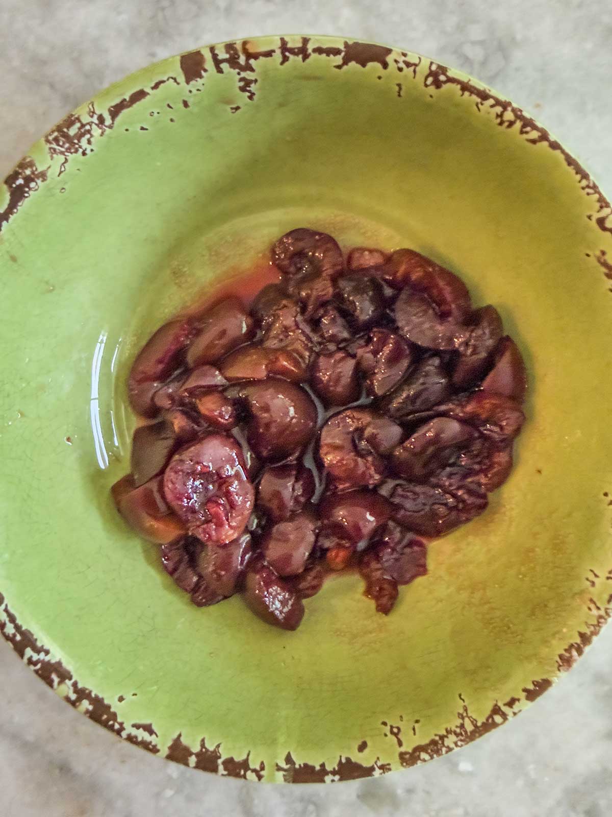 A green bowl filled with chopped frozen cherries in a small amount of broth, placed on a light-colored surface, sits next to a scoop of cherry ice cream for an unusual pairing.