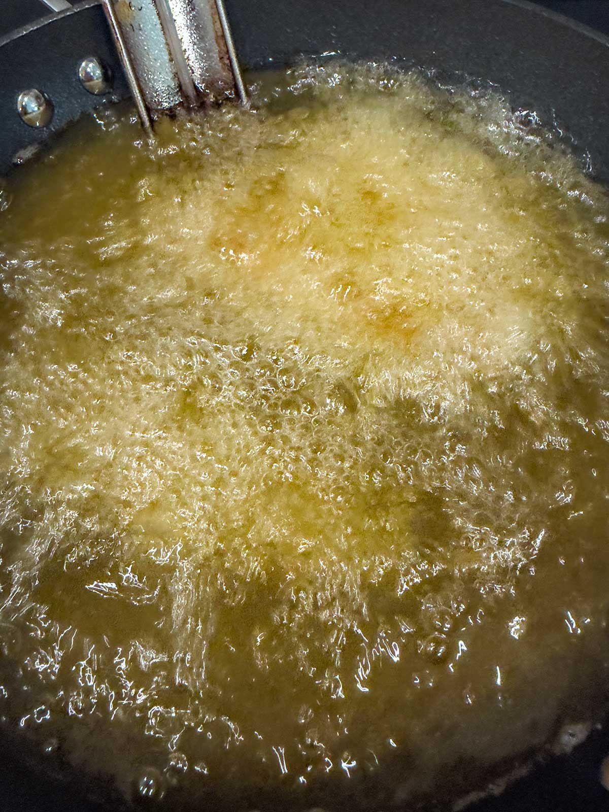 Hot oil in a frying pan with food submerged and bubbling, indicating deep frying in progress.