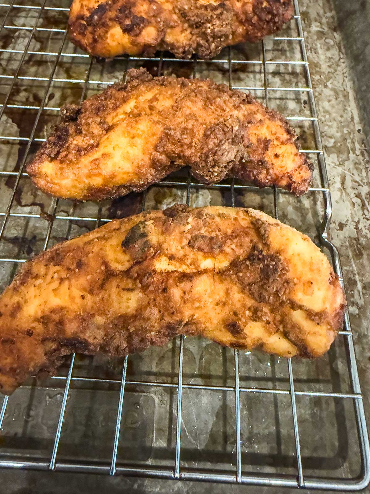 Two pieces of golden brown, crispy fried chicken resting on a metal cooling rack over a baking sheet.