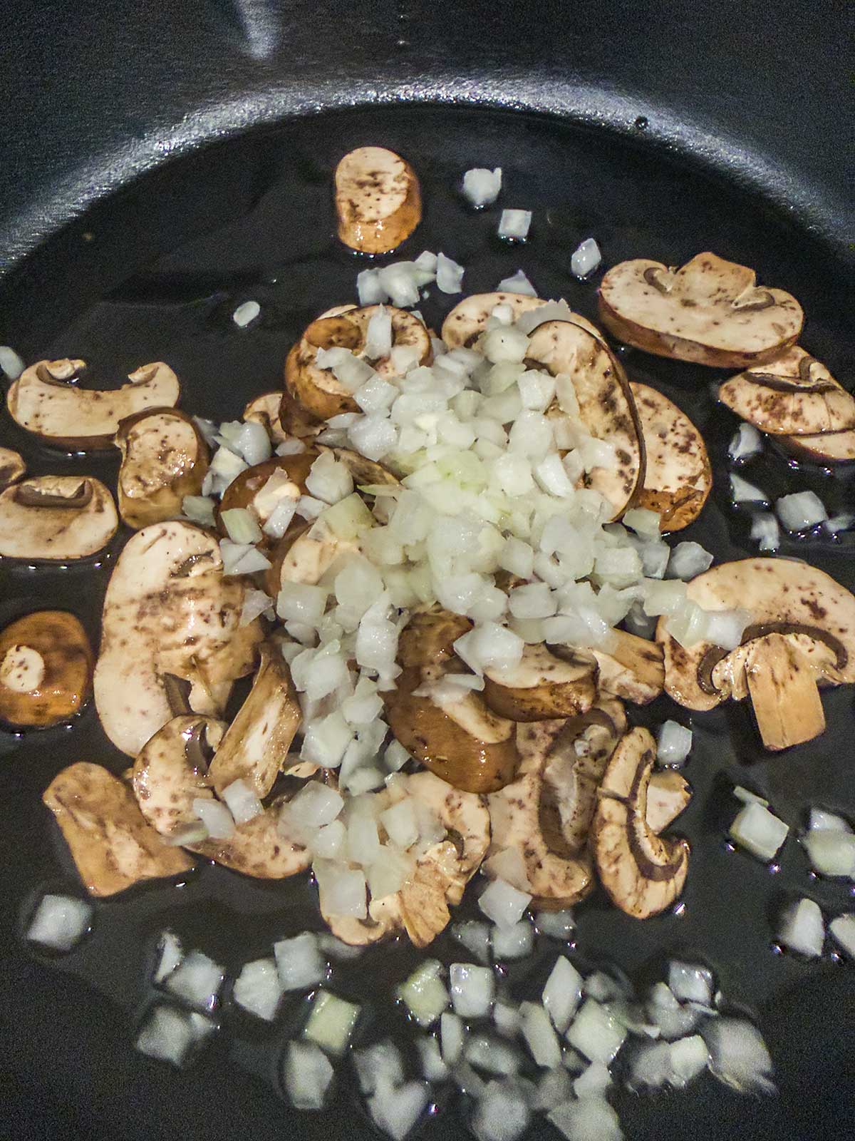 Sliced mushrooms and chopped onions in a black skillet, ready to be cooked.