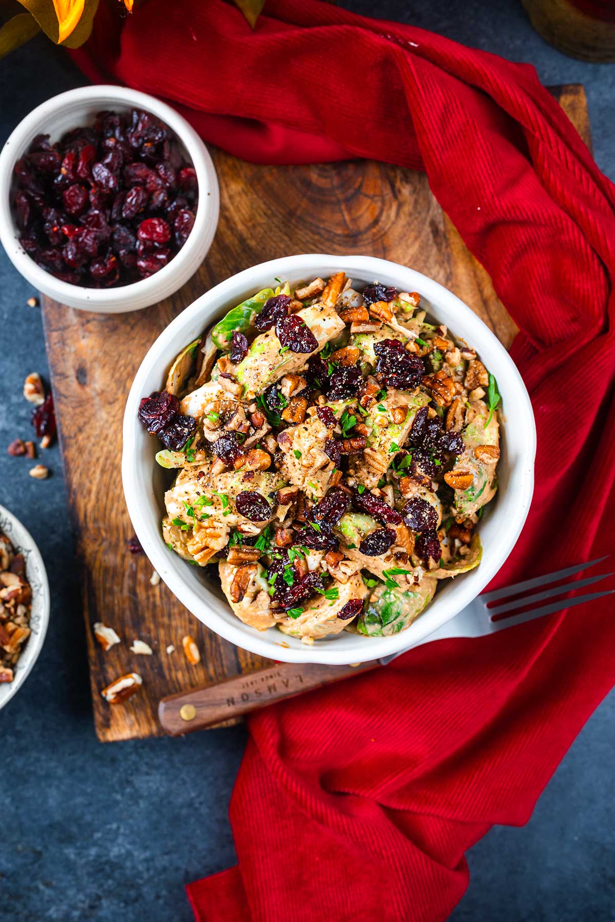 A white bowl of salad with spinach, chicken, pecans, and dried cranberries sits on a wooden board beside a small bowl of cranberries, a red cloth napkin, and a fork&mdash;perfect to pair with refreshing Ninja Creami Pumpkin Ice Cream for dessert.