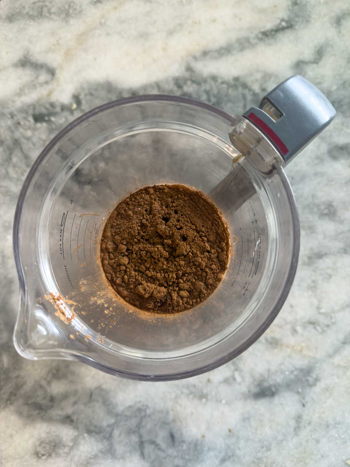 A clear measuring cup containing a mound of cocoa powder sits on a gray marble surface, ready to be used for homemade Ninja Creami chocolate ice cream.