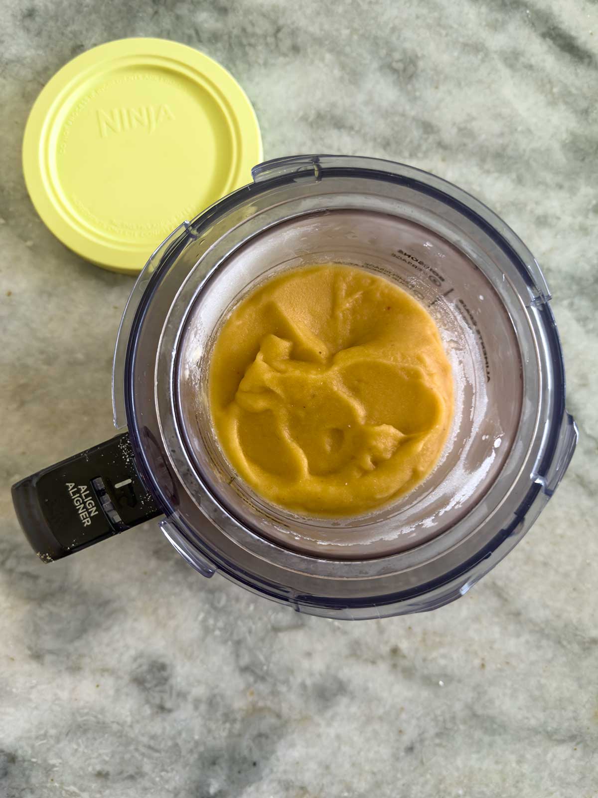 Overhead view of a creami pint with the lid off and resting to the side on a light gray countertop.