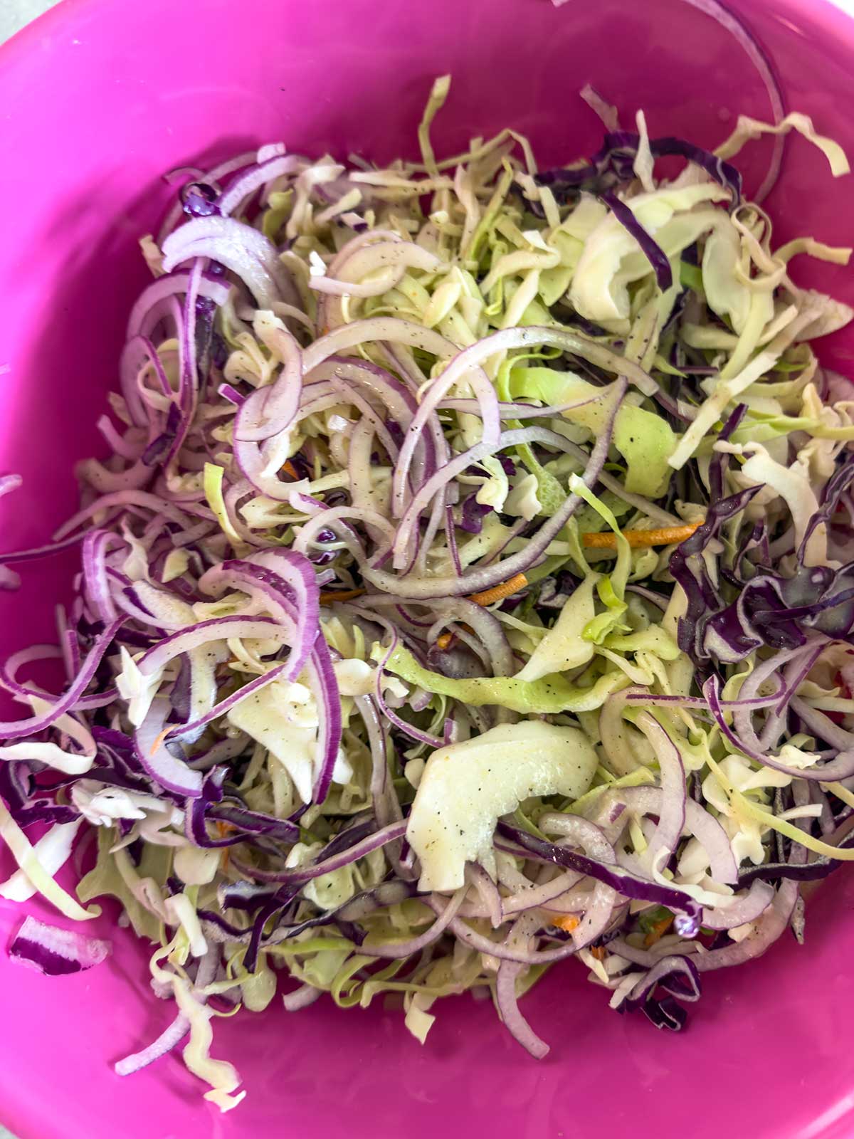 A close-up of a pink bowl filled with shredded cabbage and red onions, mixed together to make a fresh Old-Fashioned Coleslaw with Vinegar.