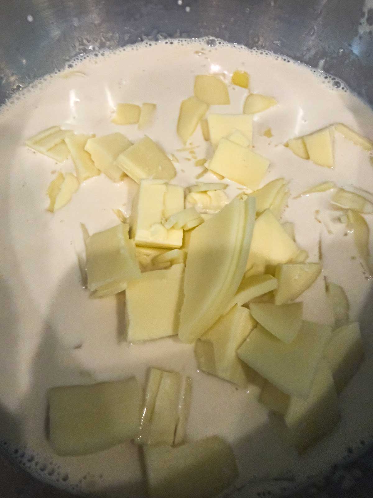 Chopped white chocolate pieces in a bowl of cream, ready to be melted and mixed, likely for a dessert preparation.