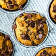 Close-up of chocolate chip muffins in a metal muffin tin, their golden-brown tops and melted chips tempting beside a scoop of Ninja Creami Pumpkin Ice Cream.