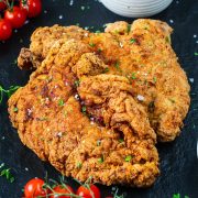 Two large, crispy, golden-brown fried chicken steaks garnished with sea salt and chopped herbs, served on a dark surface with cherry tomatoes and fresh thyme nearby—perfect before enjoying Ninja Creami Pumpkin Ice Cream for dessert.