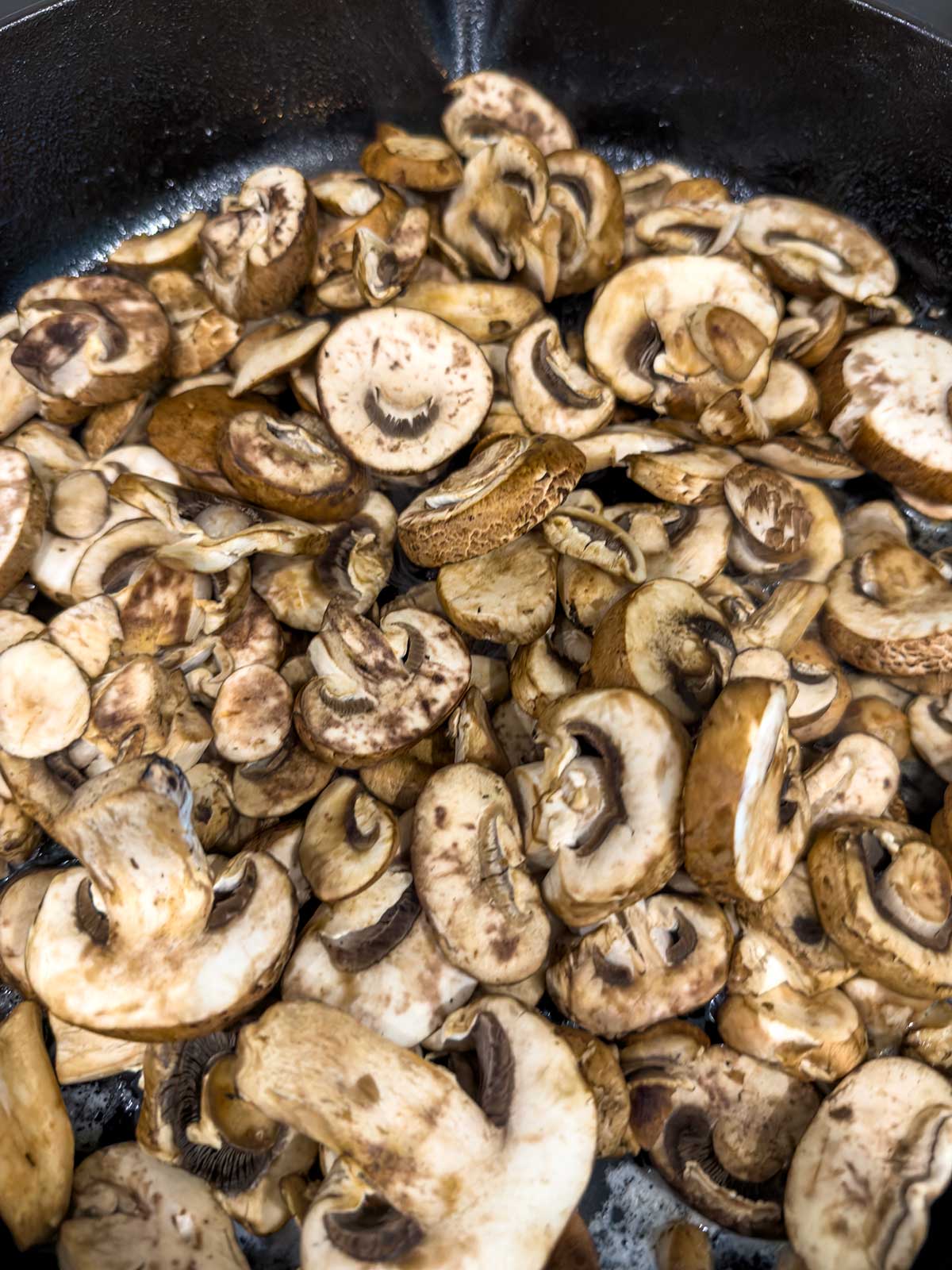 A close-up of Sautéed Mushrooms for Steak sizzling in a black skillet, highlighting their browned edges and textured surfaces.