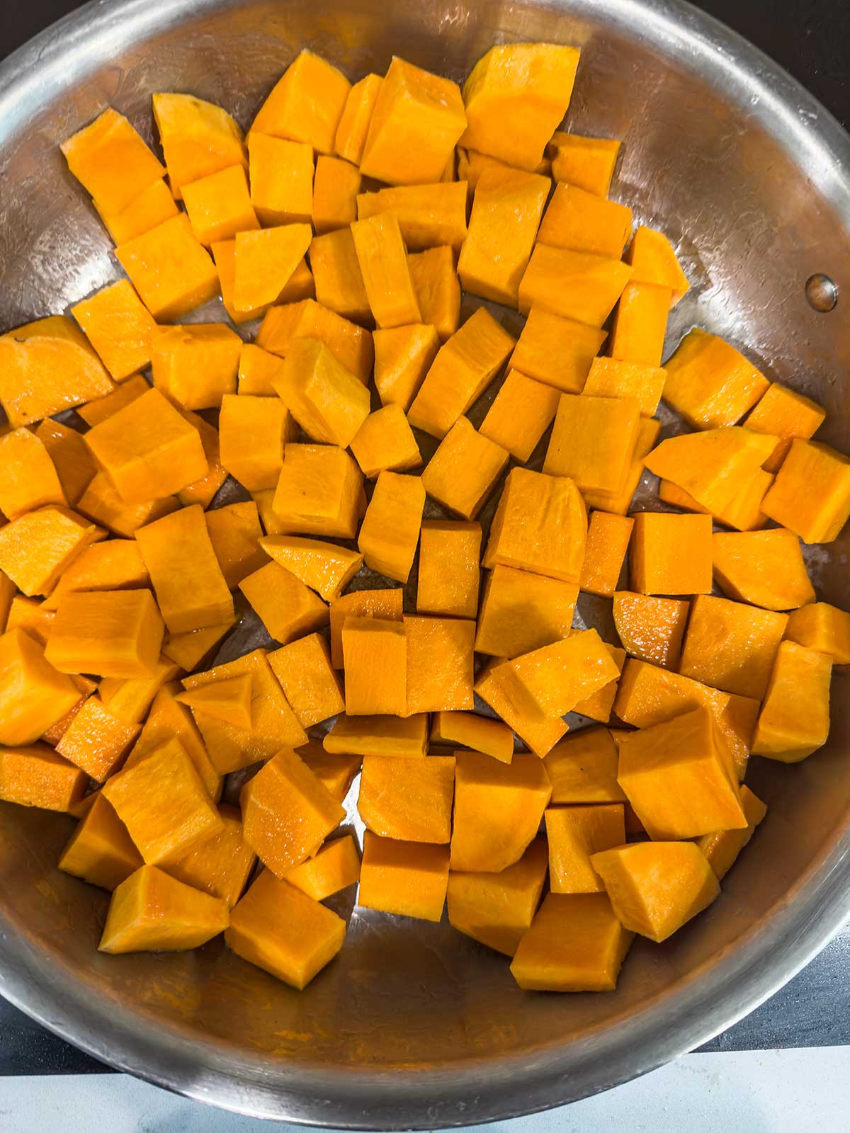 Cubed pieces of raw sweet potato spread out evenly in a large stainless steel pan, ready for cooking.