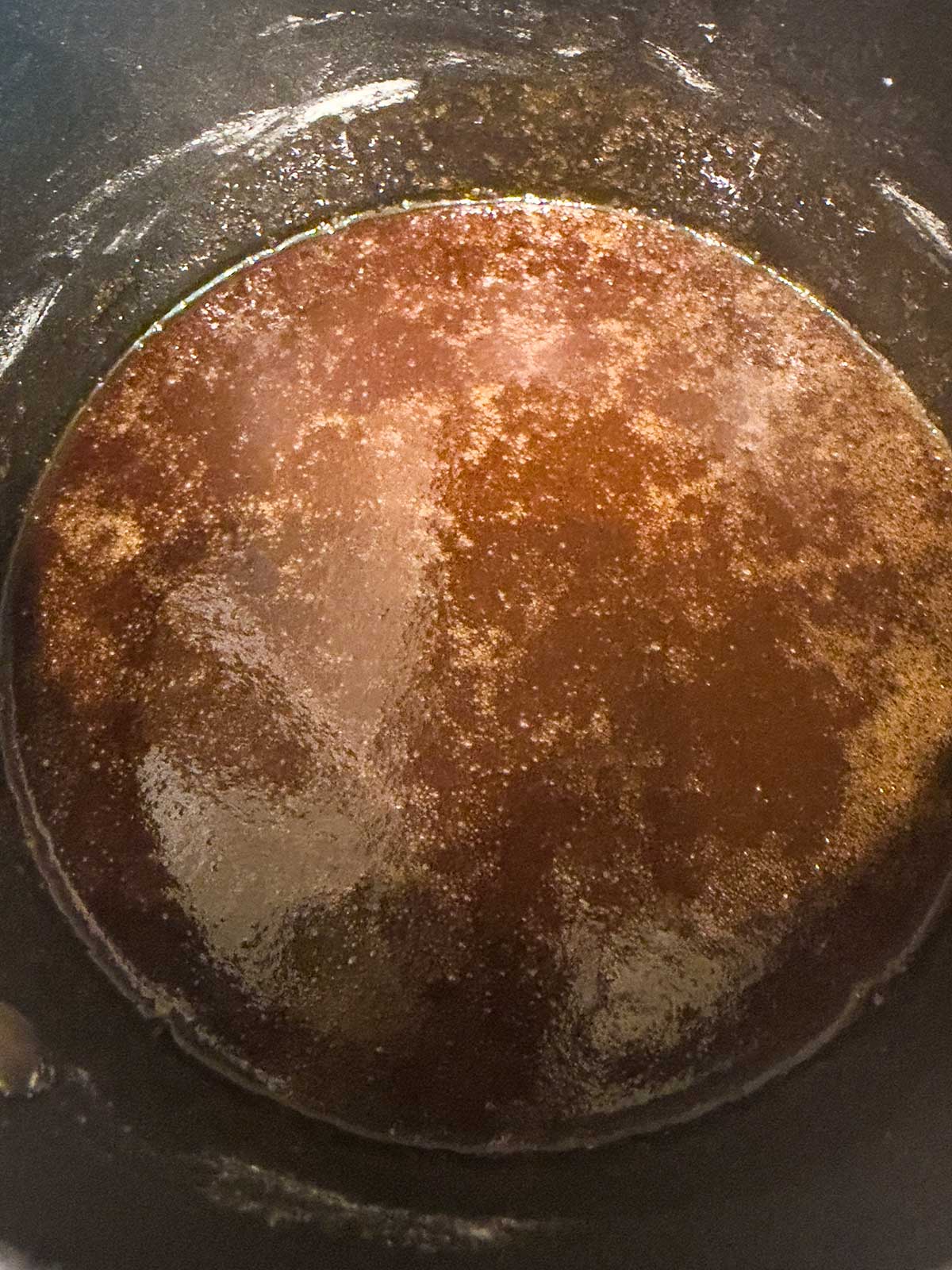 A close-up view of a pot containing melted brown butter, with a golden-brown color and a slightly frothy surface.