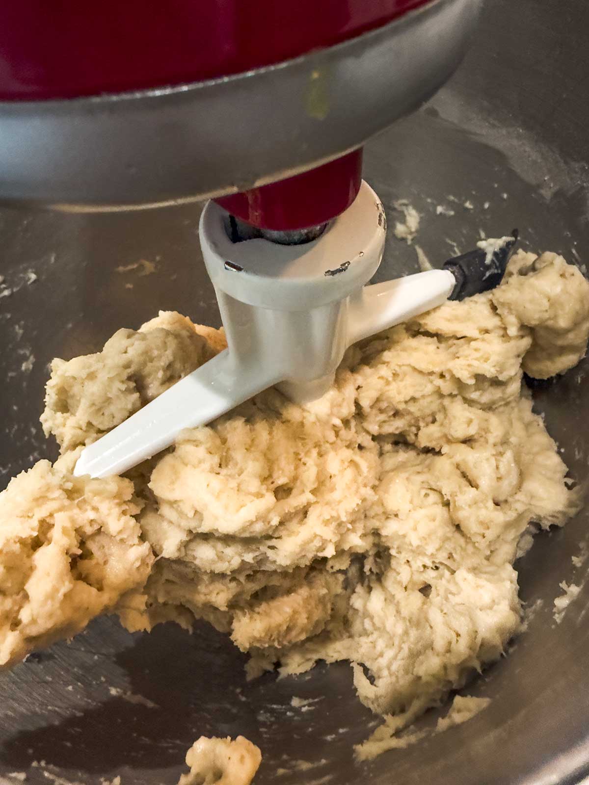 A stand mixer with a paddle attachment mixing thick, pale dough in a metal bowl.