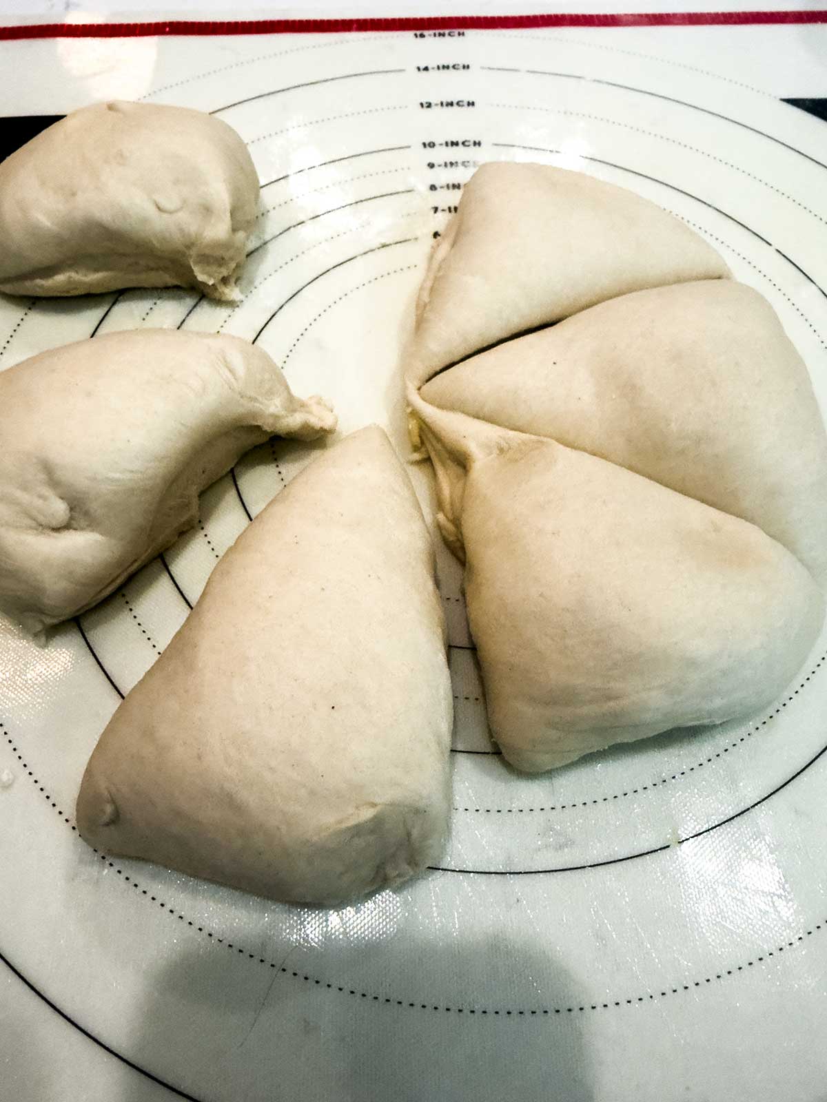 Six pieces of dough sit on a circular, marked, nonstick pastry mat, ready to be shaped or rolled out for baking.