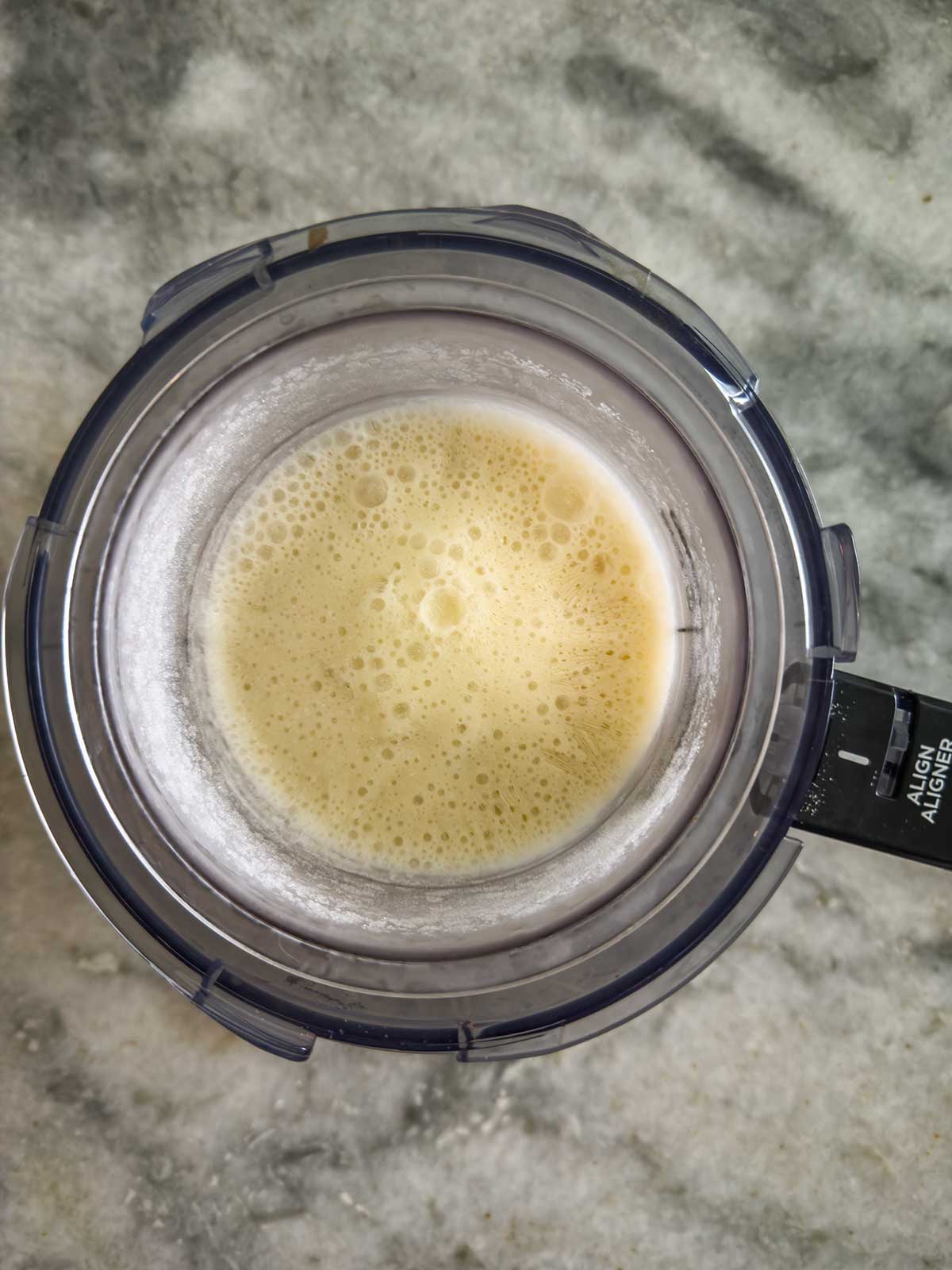 A top-down view of a Ninja Creami pint filled with ninja creami frozen yogurt, sitting on a gray marbled countertop.