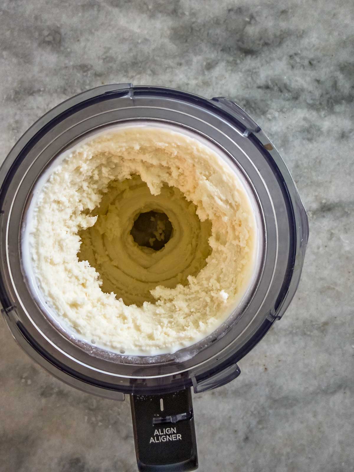 Overhead view of a Ninja Creami bowl containing thick, creamy whipped butter with a hollow center, placed on a gray marble countertop—perfect alongside homemade Ninja Creami frozen yogurt.