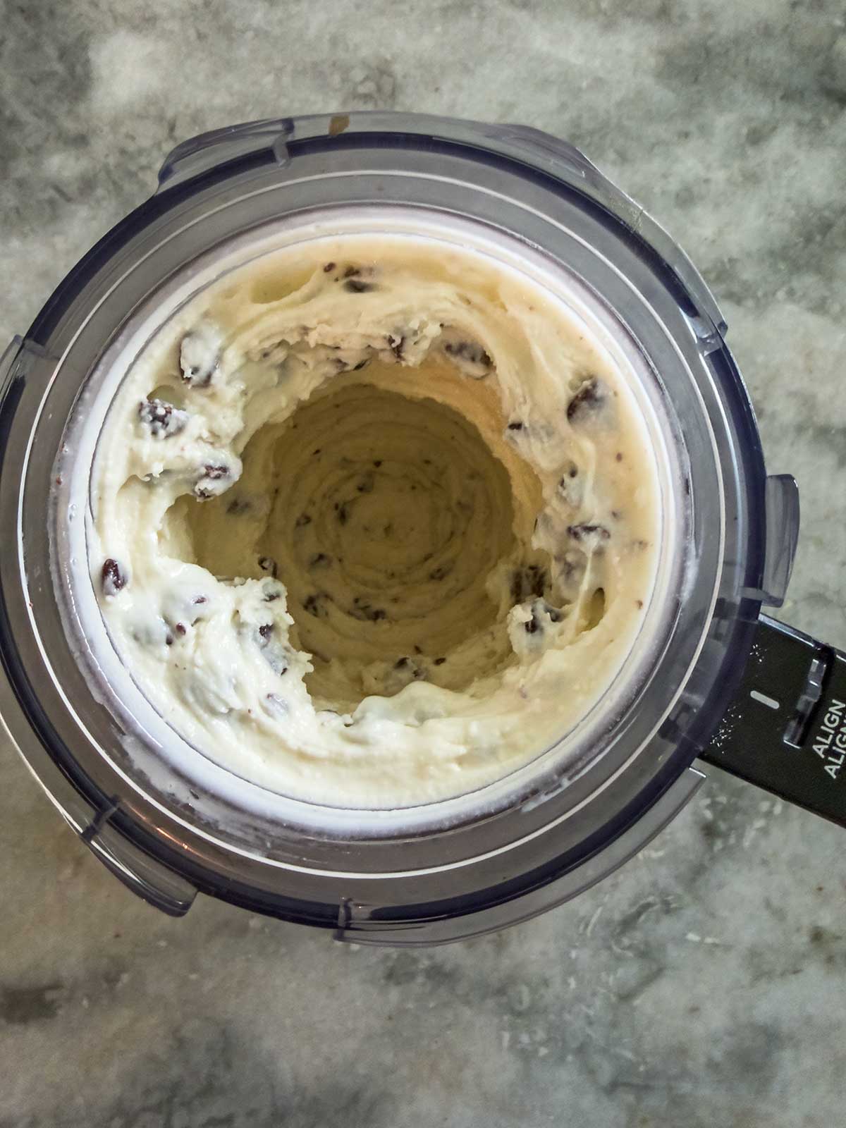 A top-down view of a Ninja Creami food processor containing freshly blended, creamy vanilla frozen yogurt with chocolate chips, featuring a hollow center and some ice cream clinging to the sides.