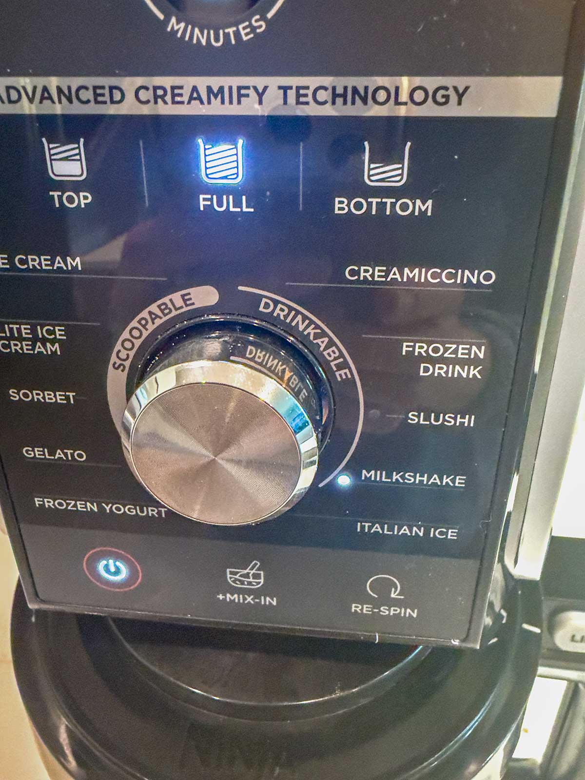 Ninja Creami machine close up showing options like Gelato, Sorbet, Frozen Yogurt, and a large dial with Scoopable and Drinkable settings.