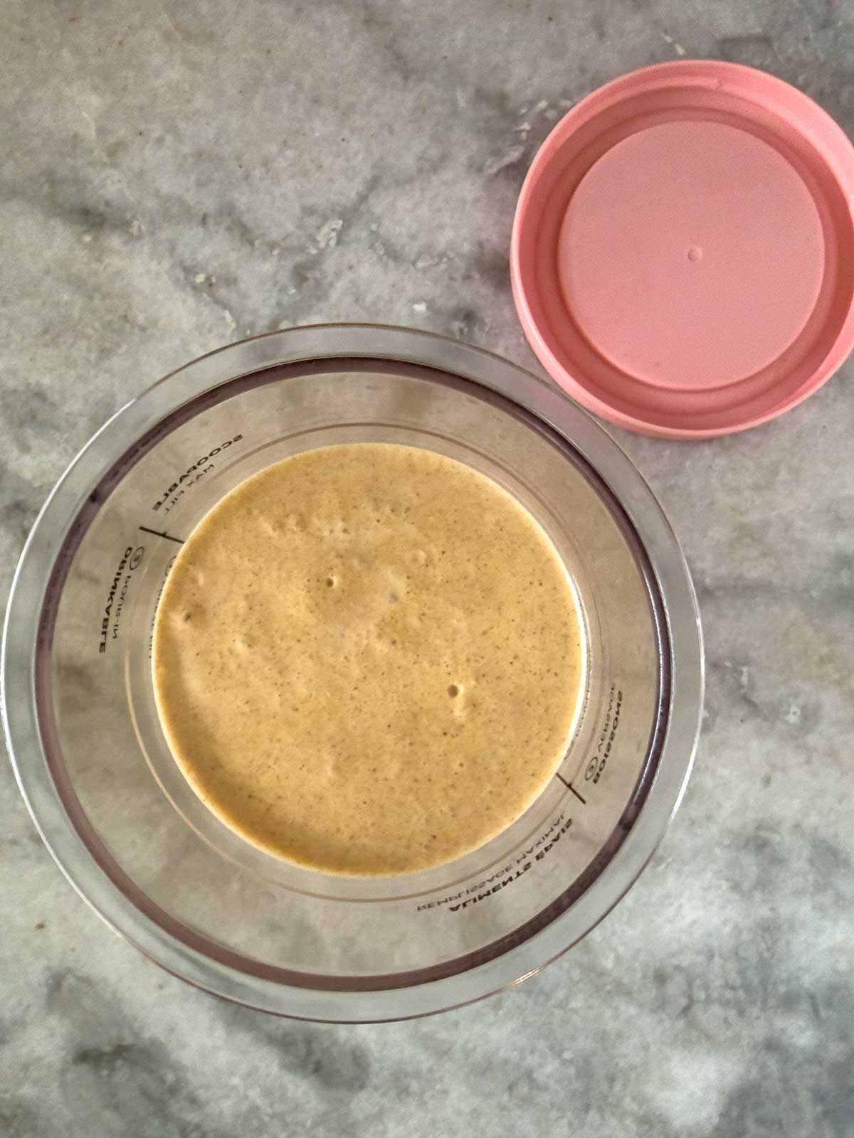 A homemade Ninja Creami Pumpkin Ice Cream in a Creami containter. A pink plastic lid is placed beside the bowl.