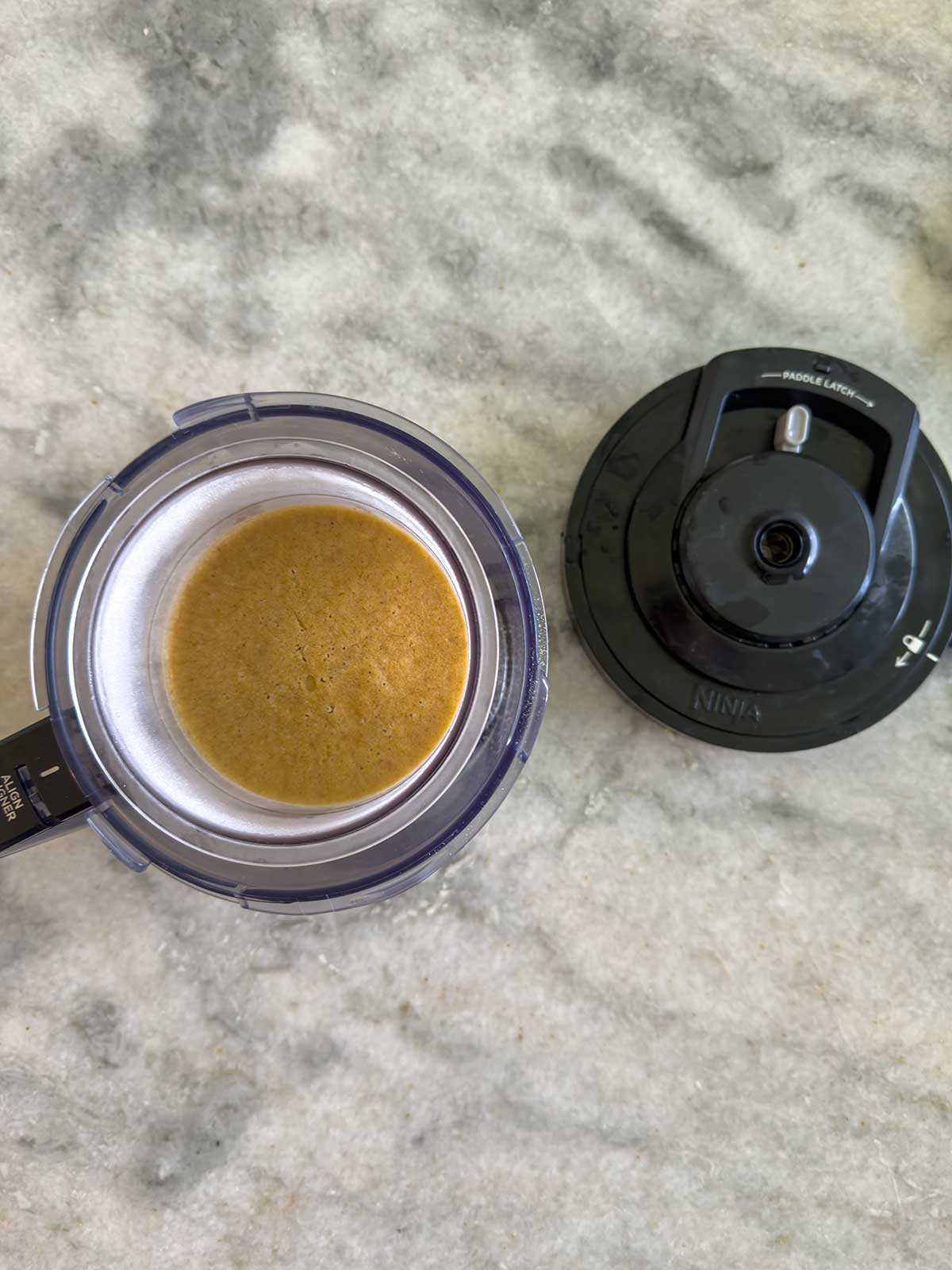 Ninja Creami Pumpkin Ice Cream, sits next to a black Ninja creami lid on a gray marble countertop.